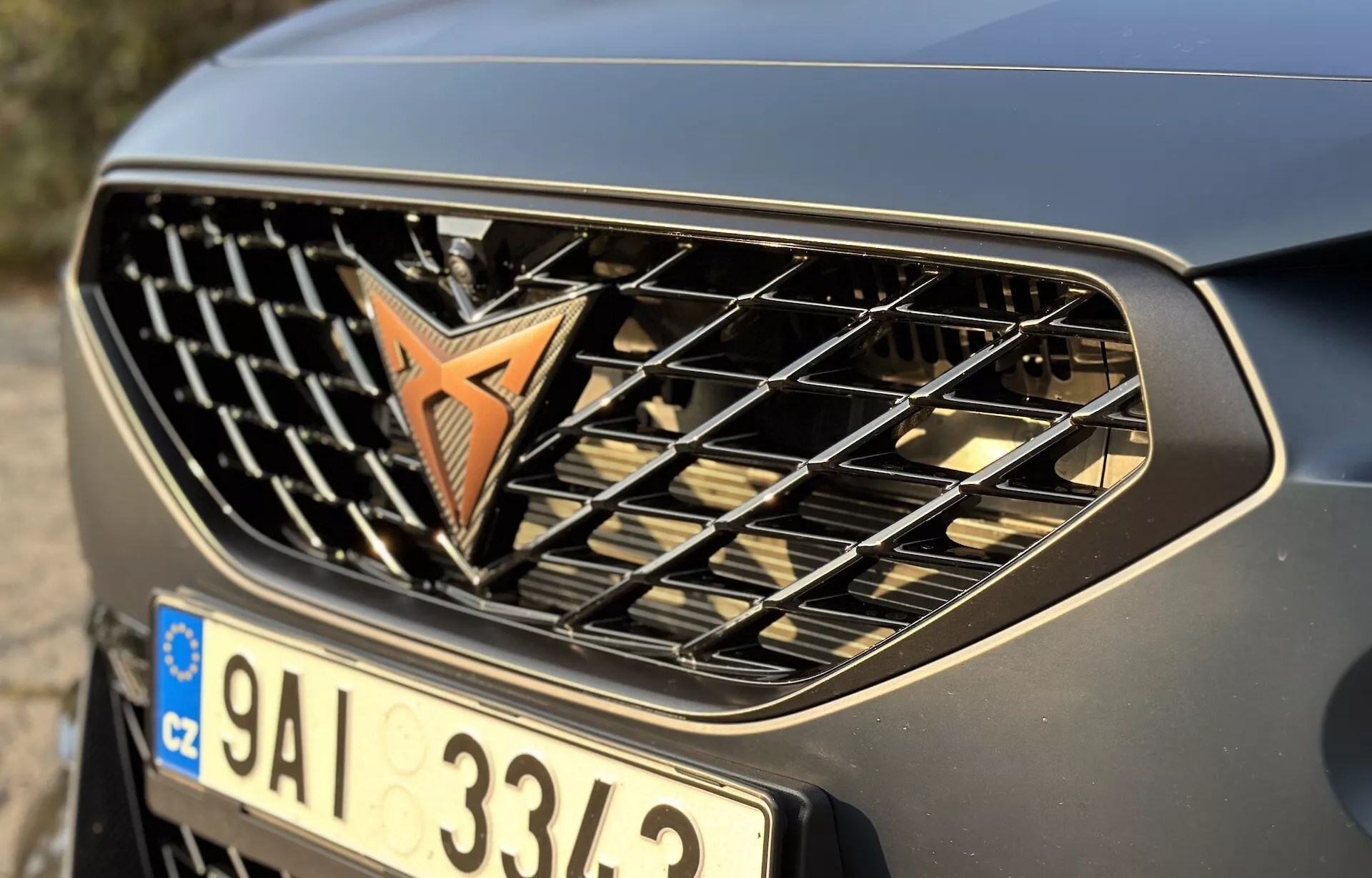 Vista de cerca de la parrilla delantera y el parachoques del Cupra Formentor 2020 mostrando el emblema, barras horizontales y un acabado metálico, enfatizando su diseño automotriz y marca
