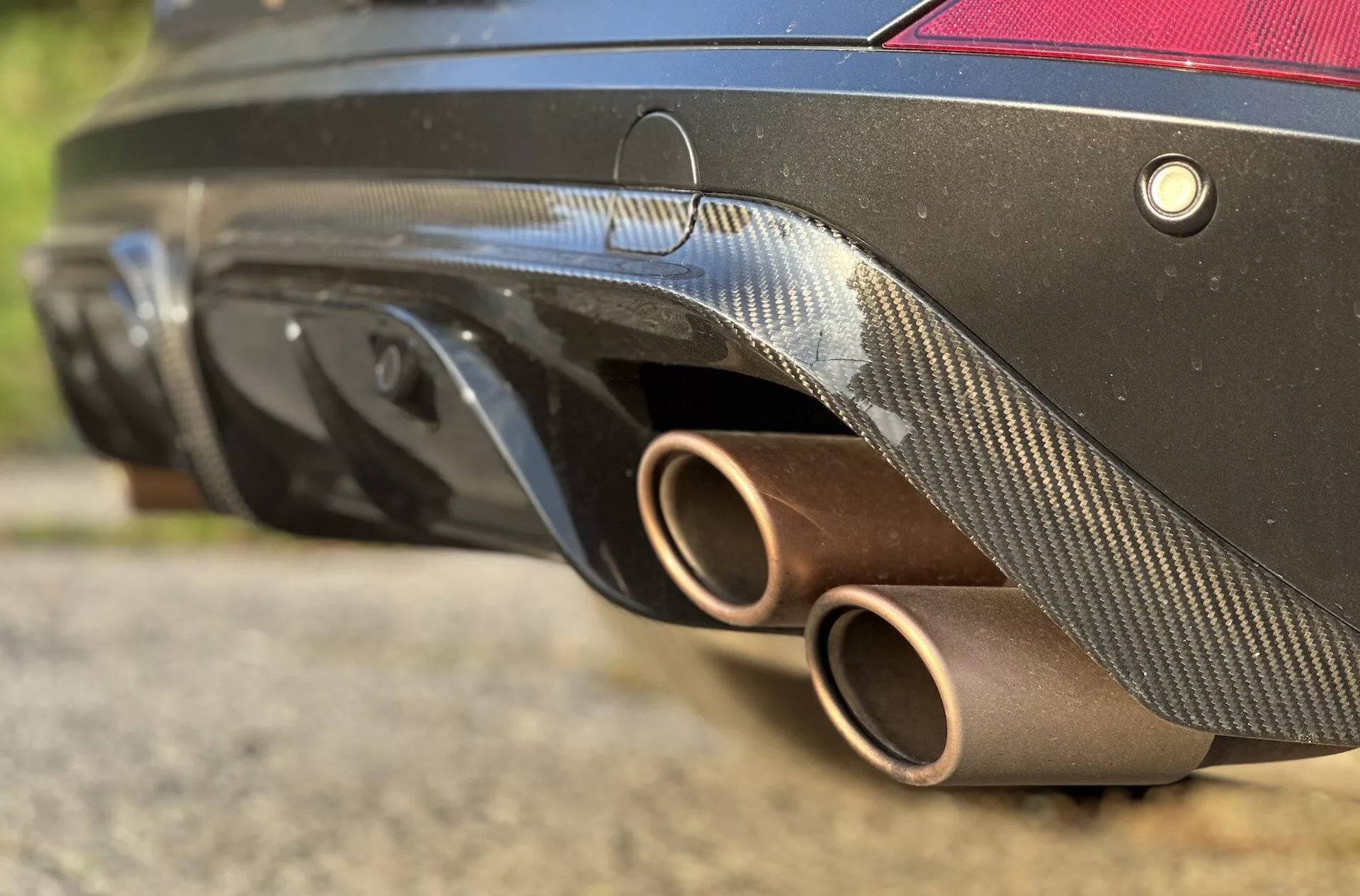 Vista detallada de la parte trasera del Cupra Formentor 2020, mostrando los tubos de escape bronce, el difusor de fibra de carbono, el sistema de sensores y el color negro del cuerpo desde un ángulo bajo que enfatiza su diseño deportivo y características de rendimiento