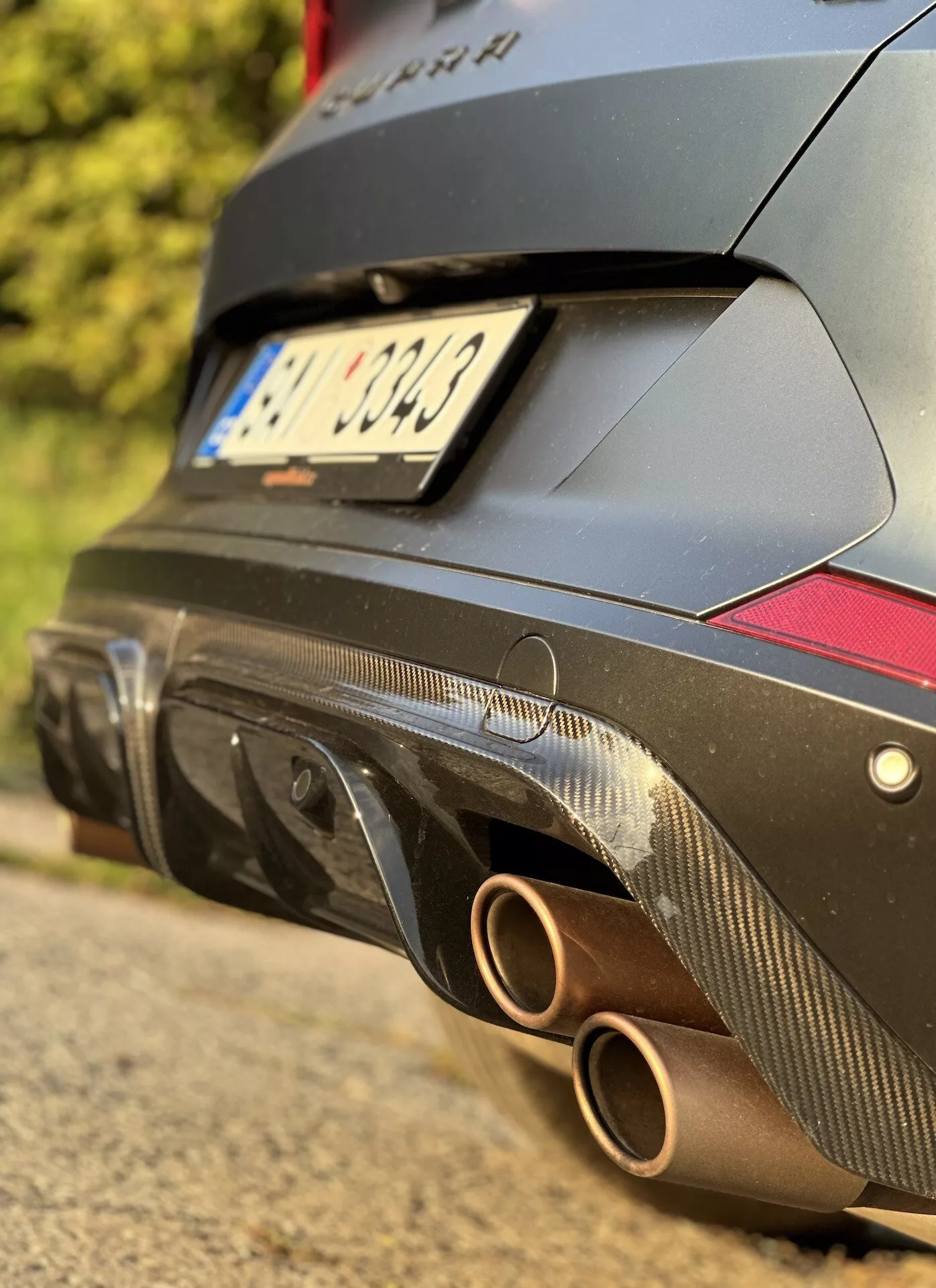 Vista cercana de la sección trasera del Cupra Formentor 2020, enfocando al sistema de escape con dos colas redondas y difusor de fibra de carbono con reflectores rojos, contra un cuerpo de diseño orientado al rendimiento de color oscuro.