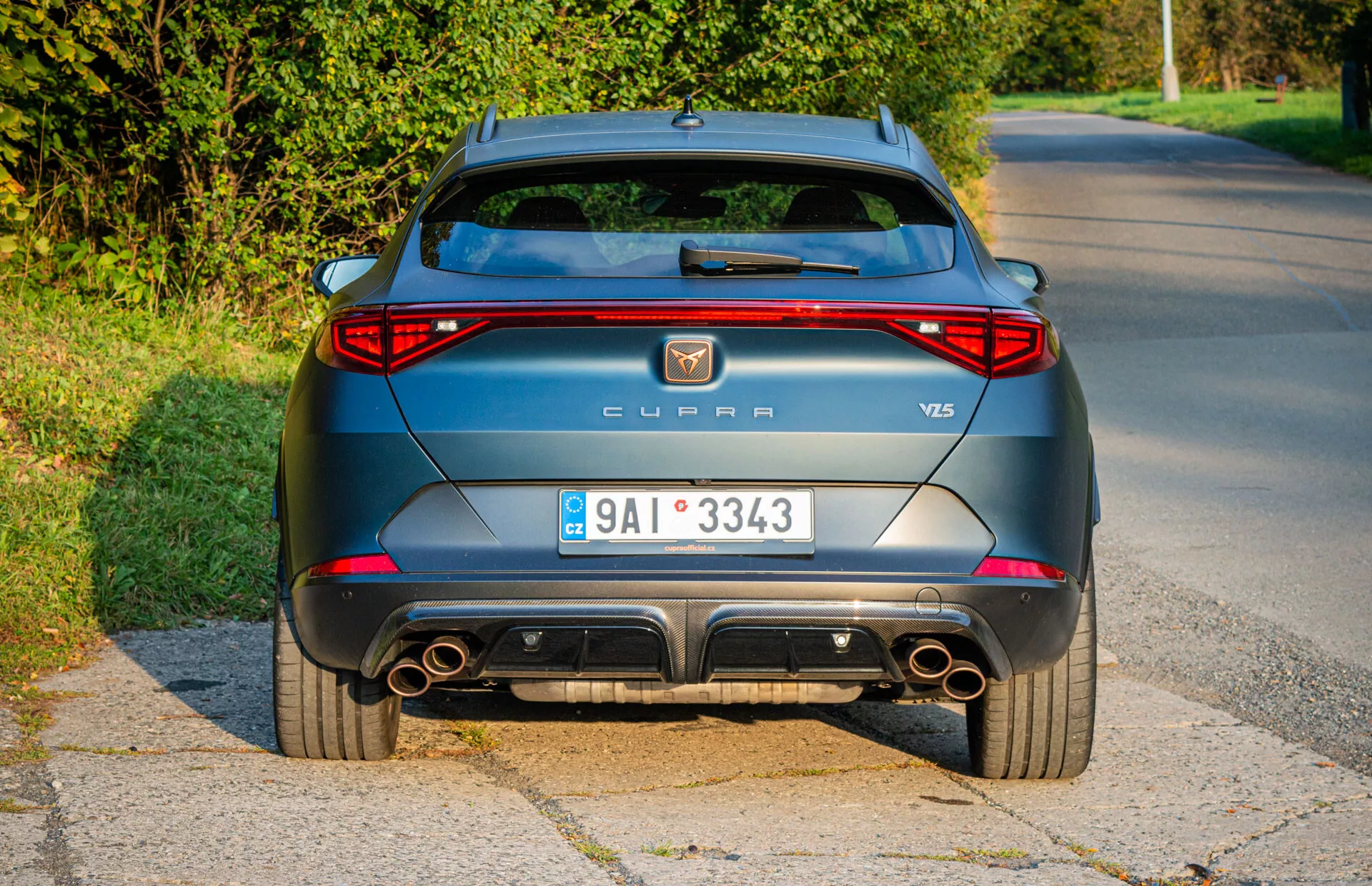 Vista trasera de un CUPRA Formentor VZ5 de 2020 en gris metálico estacionado al lado de una carretera, mostrando luces traseras LED, escapes dobles y características de diseño aerodinámico durante una toma de luz diurna de última hora de la tarde