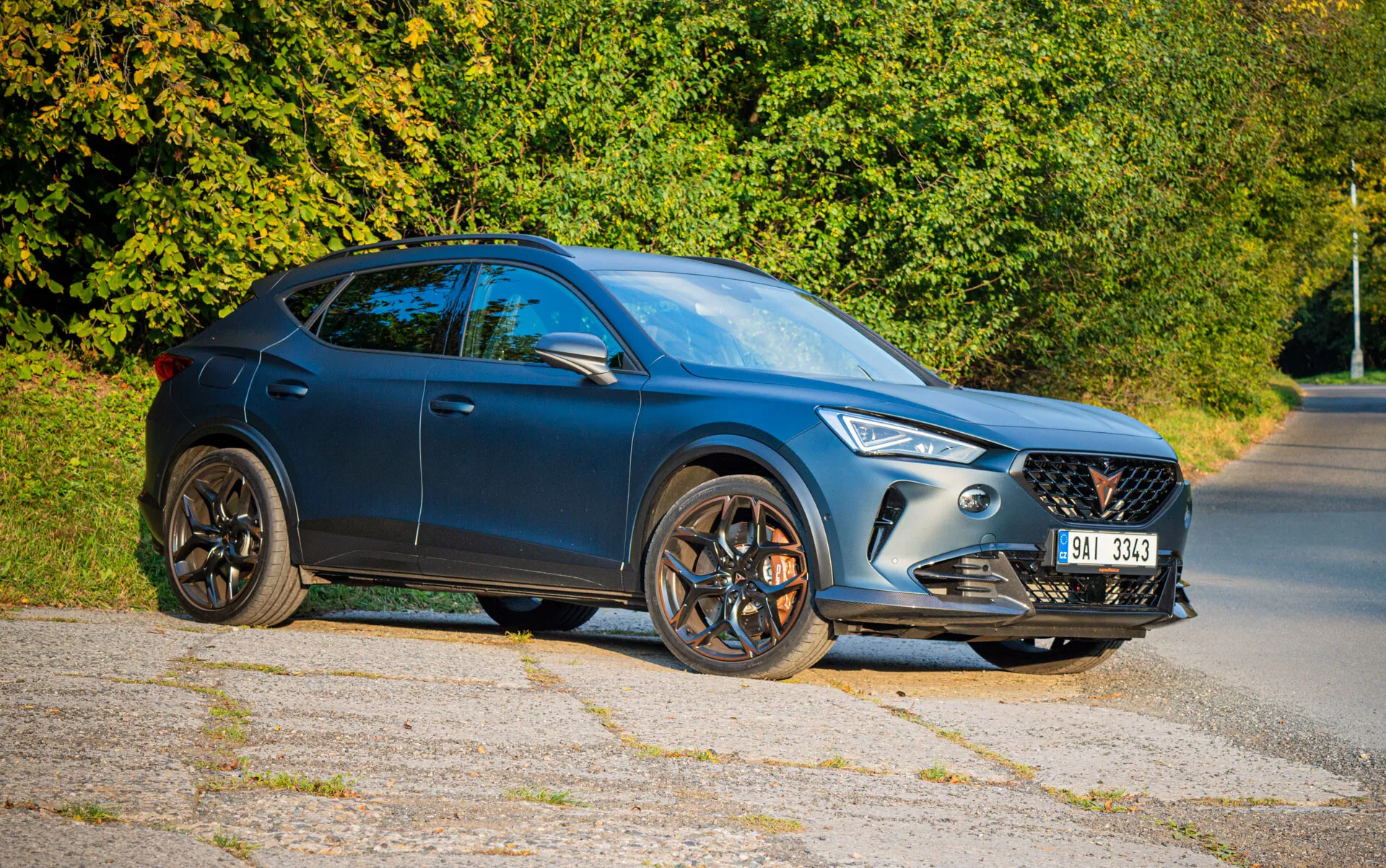 SUV crossover Cupra Formentor 2020 en azul oscuro, con diseño elegante, faros LED y llantas de aleación de cinco radios, fotografiado desde un ángulo frontal de tres cuartos en una carretera suburbana