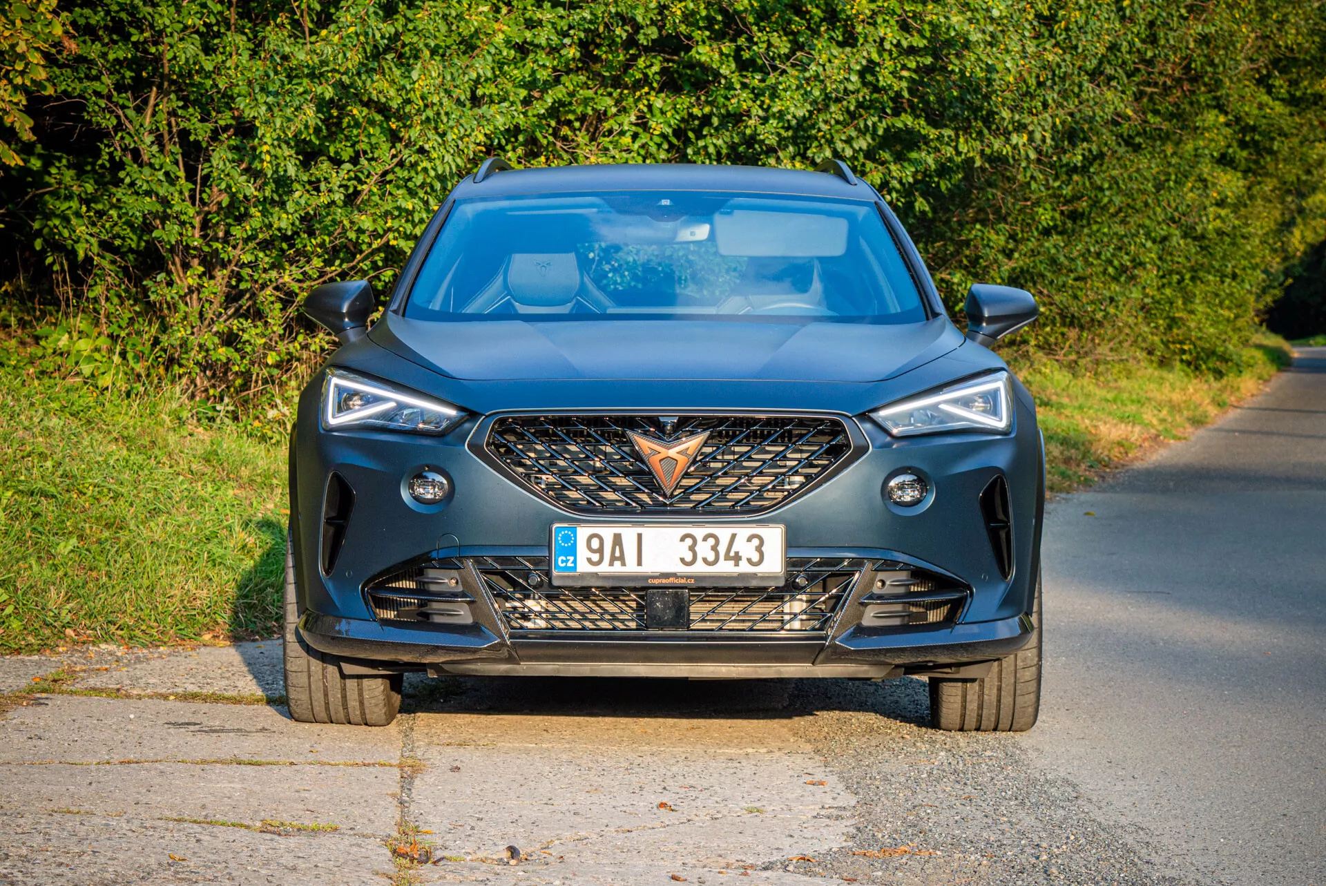 Vista frontal moderna del Cupra Formentor 2020 en camino pavimentado con luz natural diurna y fondo rural, destacando la parrilla agresiva, faros LED afilados, contornos dinámicos del capó y características de tecnología avanzada