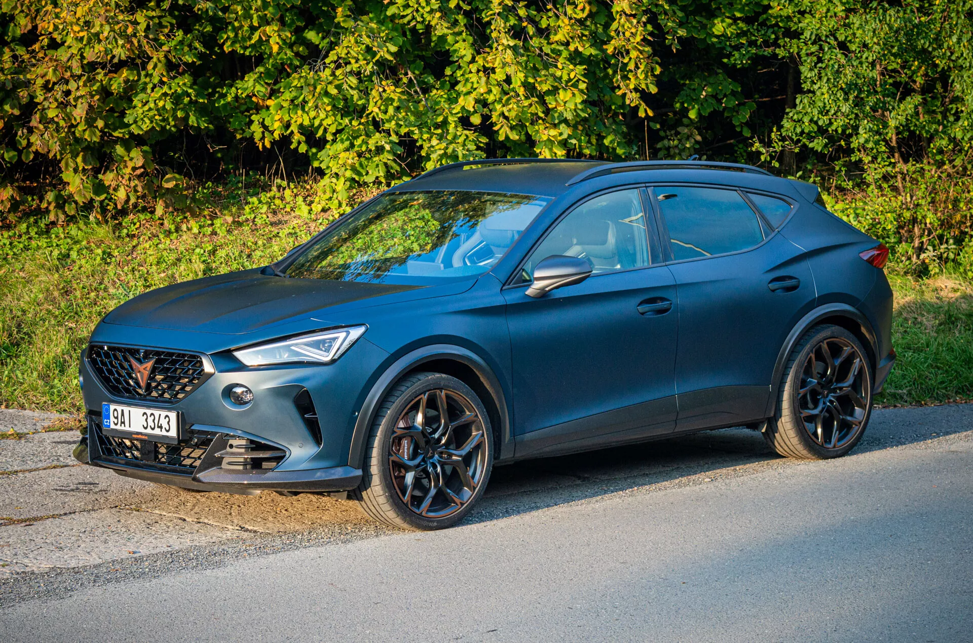 SUV crossover azul Cupra Formentor 2020 aparcado al lado de la carretera con vegetación de fondo, destacando la vista frontal de tres cuartos enfocada en el lado del conductor, parrilla frontal, faros angulares, ruedas de aleación de múltiples radios y perfil lateral tipo coupé deportivo