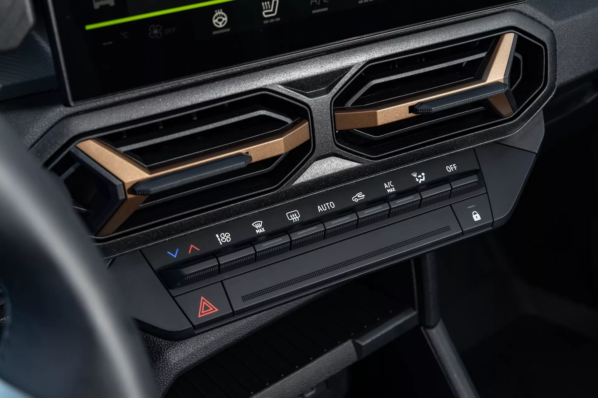 Vista detallada del sistema de control climático en el Dacia Duster 3ra generación 2024 en el tablero central bajo la pantalla de infotenimiento, mostrando ajustes de temperatura y velocidad del ventilador, funciones de distribución de aire, características de deshielo, botón de luces de emergencia, y opciones de aire acondicionado, enmarcado por rejillas de ventilación angulares y acentuado con un borde metálico para una estética interior moderna