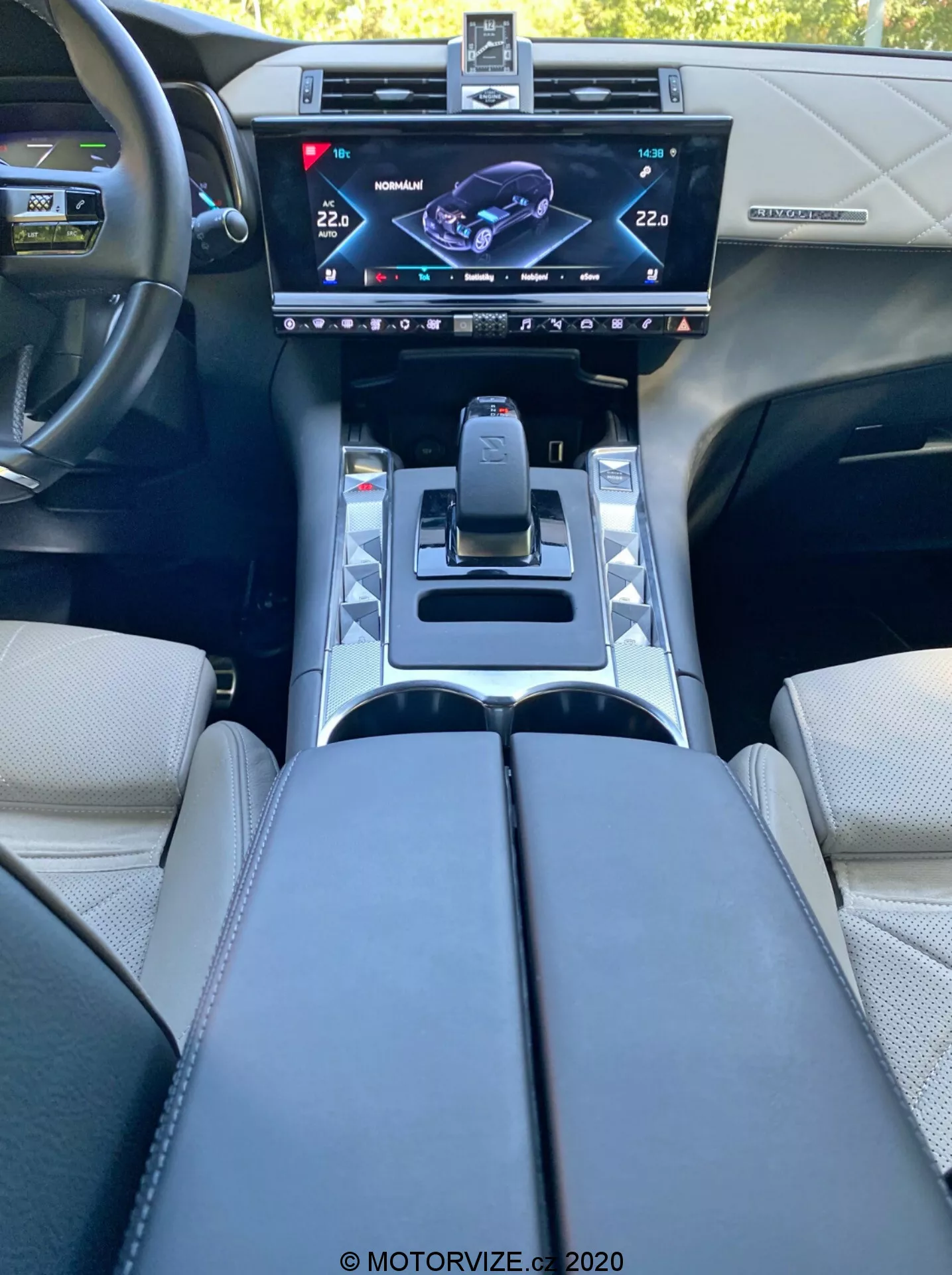 Vista interior del DS Automobiles DS 7 Crossback 2018 desde el asiento del conductor, mostrando la consola central con una pantalla táctil de infotainment de alta resolución, selector de marchas moderno, botones de modos de conducción, portavasos, reposabrazos tapizados y volante con botones de control, reflejando un diseño y tecnología automotriz de vanguardia.