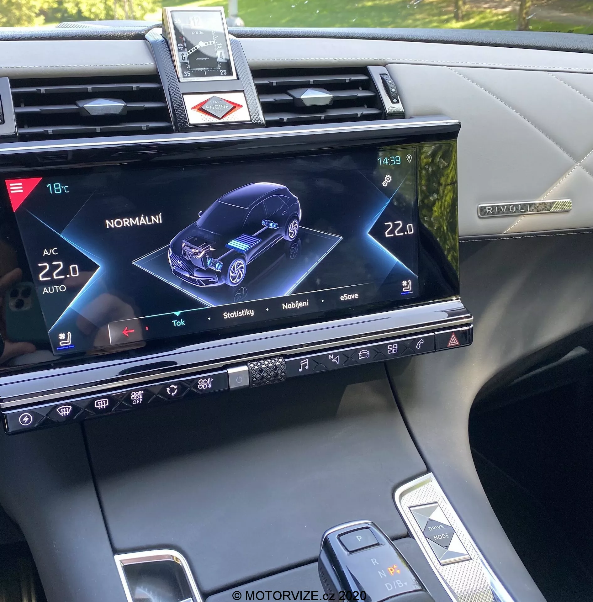 Consola central del DS Automobiles DS-7 Crossback 2018, mostrando la pantalla del sistema de infoentretenimiento con una representación gráfica 3D del coche desde una perspectiva frontal derecha, indicando el estado y varios ajustes como el control de clima, calefacción de asientos y funciones del modelo de coche interactivo, junto con botones físicos, controles táctiles y una vista parcial del selector de marchas y del modo de conducción.