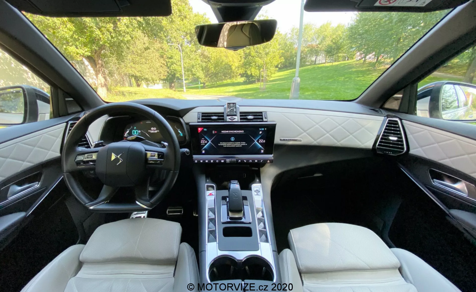 Imagen del interior del DS Automobiles DS 7 Crossback 2018 desde el asiento trasero, destacando el volante multifuncional de cuero, el panel de instrumentos digital, la pantalla táctil central de infoentretenimiento, el panel de control de clima, el selector de marchas electrónico, los asientos de cuero con costuras de diamante y la consola central con portavasos. La imagen muestra una combinación de tecnología de alta gama y diseño sofisticado.