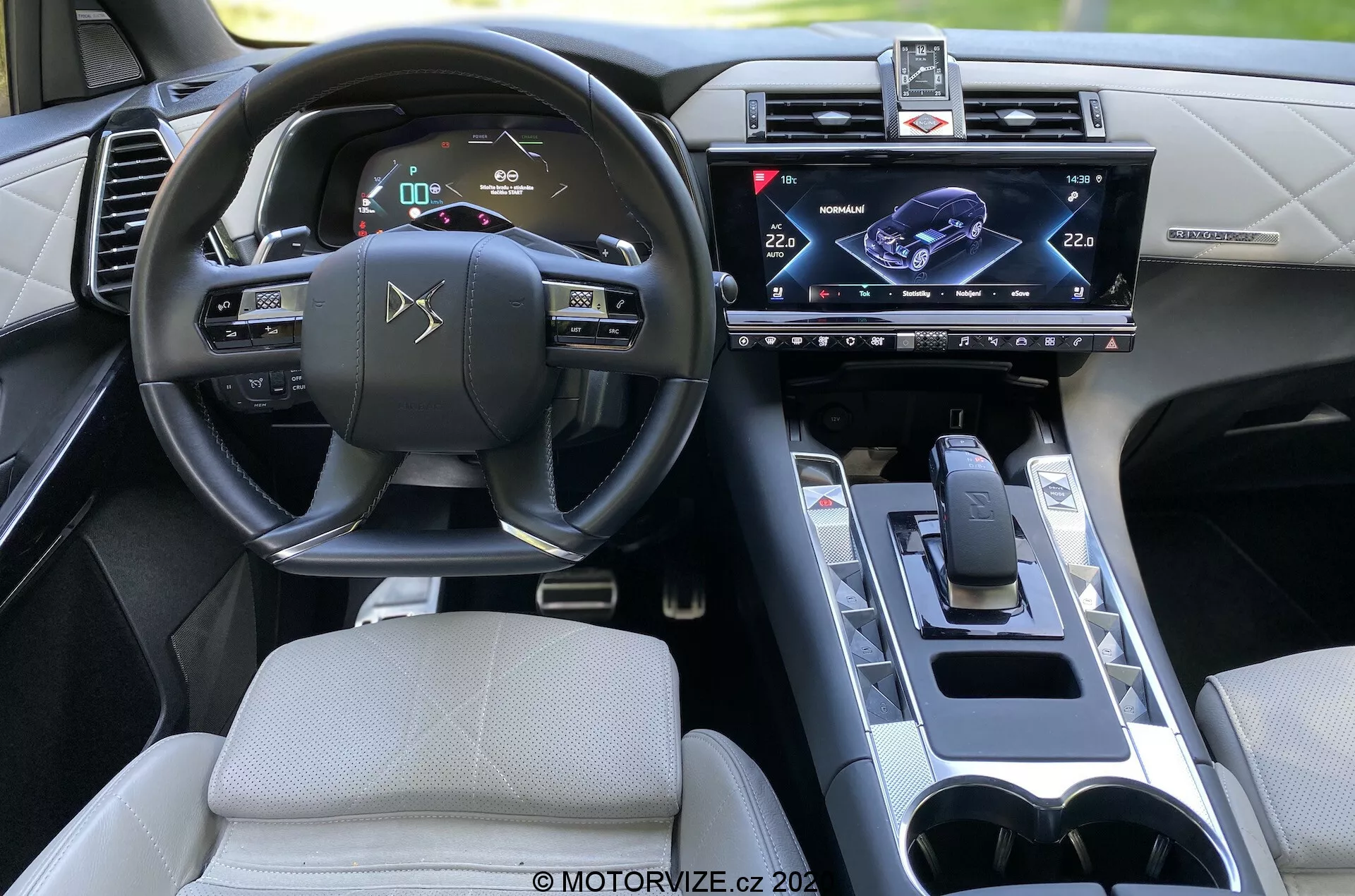 Interior del DS Automobiles DS 7 Crossback 2018, vista desde el asiento trasero enfocada al lado del conductor. Las características incluyen un volante con controles integrados, un panel de instrumentos digital, sistema de infoentretenimiento con pantalla táctil montada centralmente, palanca de cambios moderna, posavasos y un diseño interior sofisticado con comodidades tecnológicas avanzadas.