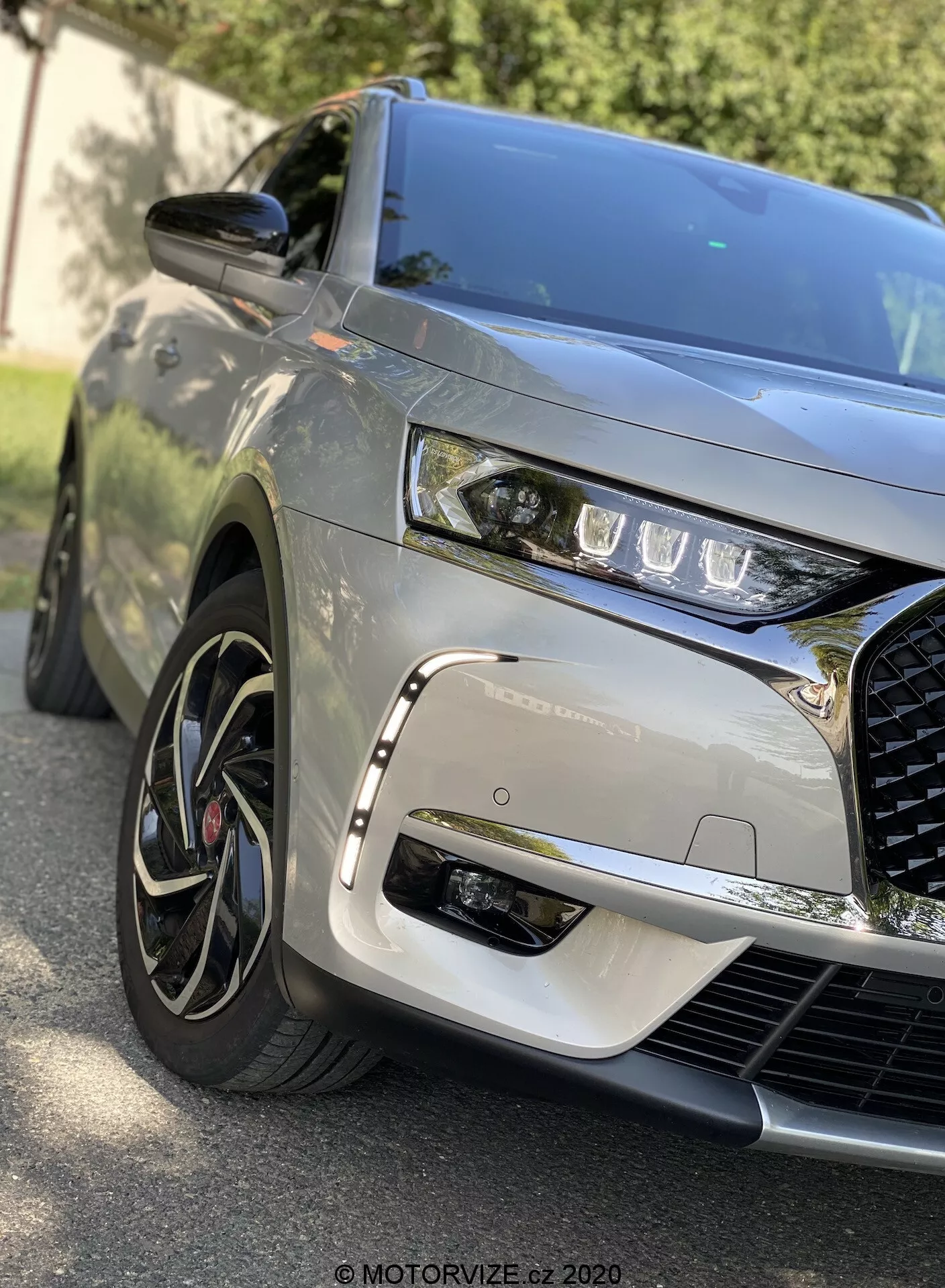 Vista cercana de ángulo frontal del DS Automobiles DS 7 Crossback 2018 que captura el cuarto delantero izquierdo, mostrando faros LED elegantes, una parrilla prominente e intrincada, capó esculpido, ruedas de aleación de múltiples radios con neumáticos de perfil bajo, acabado de pintura metálica, espejo lateral del color de la carrocería y reflejos dinámicos que indican un entorno al aire libre.