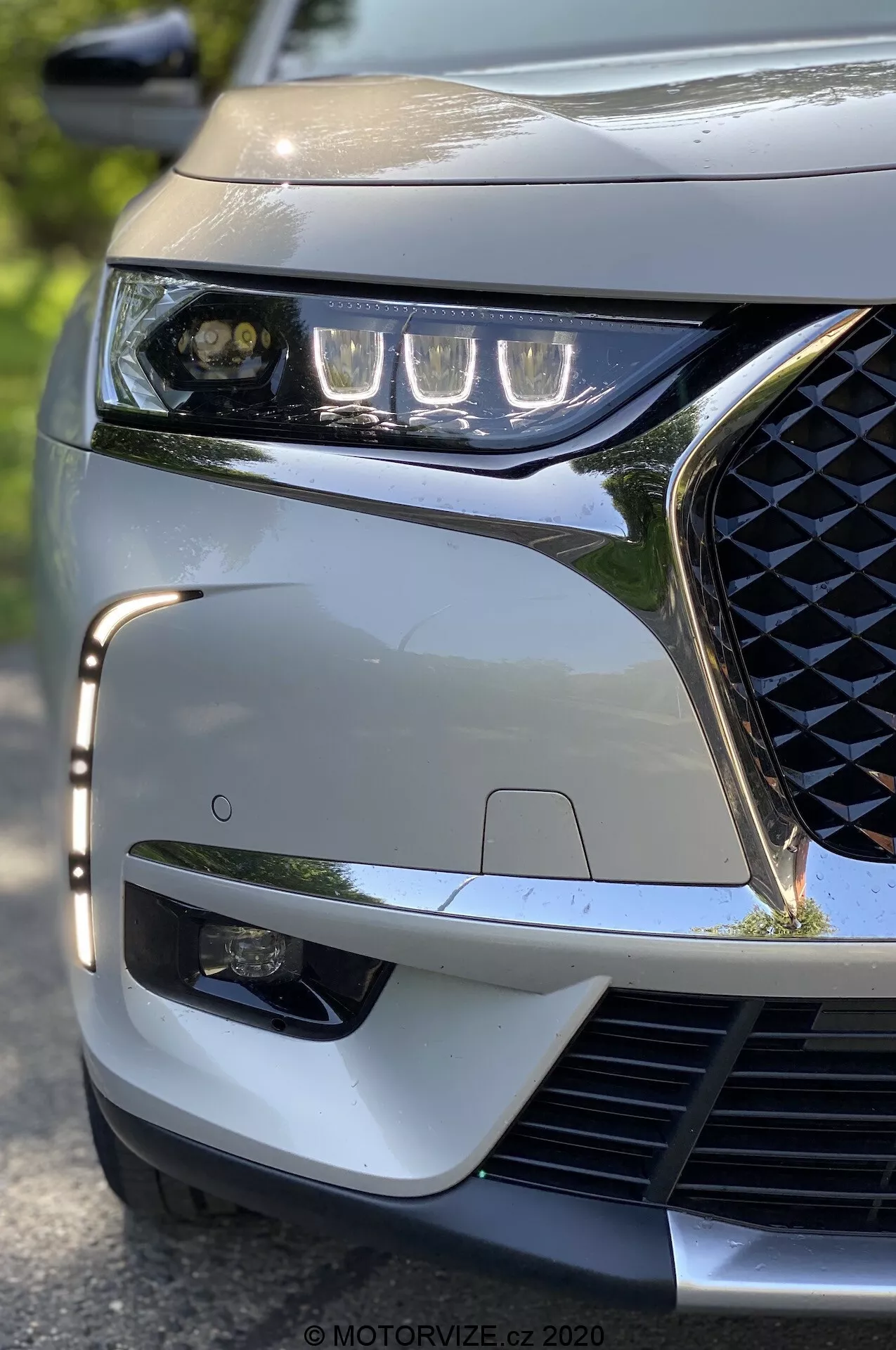 Toma de primer plano a baja altura del DS Automobiles DS 7 Crossback 2018, enfocada en el cuarto delantero izquierdo. Destacan el diseño elegante de los faros LED, la parrilla con patrón geométrico, el parachoques delantero deportivo y el sensor ADAS visible, que subrayan las características tecnológicas y estéticas modernas del vehículo.