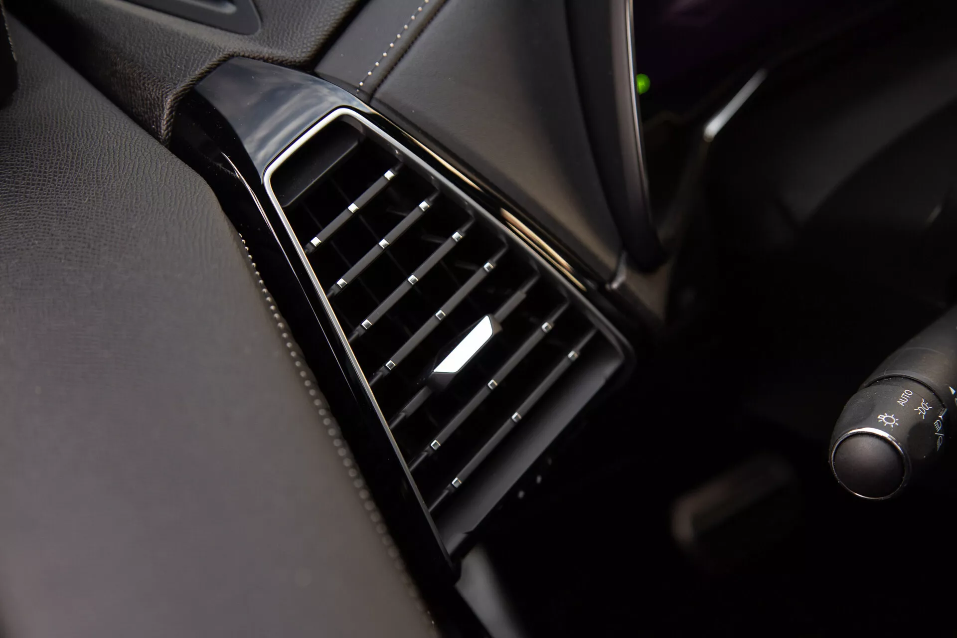 Vista de cerca de la salida de aire del DS Automobiles DS-7 2022 en el tablero con ranuras ajustables negras alineadas verticalmente, bisel brillante y un toque de plata en el control, mostrando la calidad del diseño interior y los materiales del vehículo