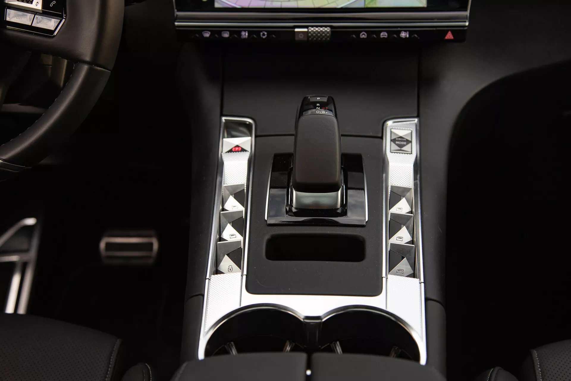 Vista detallada de la consola central del DS Automobiles DS-7 2022 con palanca de cambios ergonómica, acentos metálicos, botones de control únicos, pantalla táctil y portavasos doble, destacando elementos de control de vehículo avanzado y diseño de lujo.