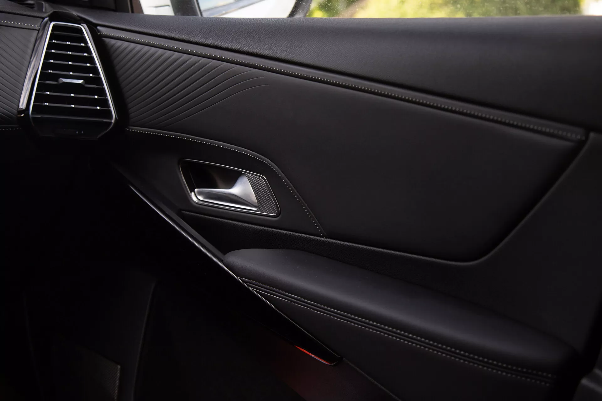 Vista detallada del panel interior de la puerta del DS Automobiles DS-7 2022, mostrando la elegante rejilla de ventilación, textura de cuero cosido, manija de puerta de cromo, palanca de cierre ergonómica, reposabrazos con costura contrastante y bolsillo de almacenamiento integrado con rejilla de altavoz parcialmente visible, reflejando calidad premium y detalles de diseño.