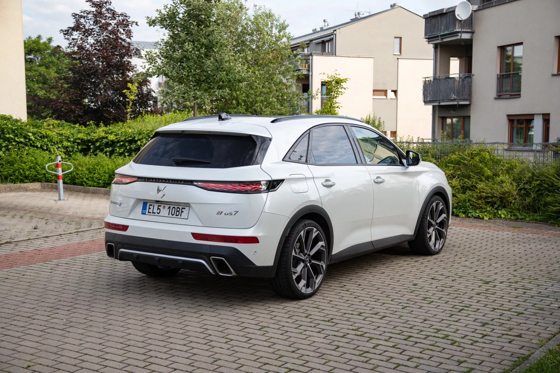 SUV blanco DS Automobiles DS-7 2022 aparcado sobre un área pavimentada con ladrillos, mostrando luces traseras LED, un sistema de escape doble y llantas de aleación deportivas. La imagen capta el diseño elegante del vehículo tipo SUV coupé desde una perspectiva trasera de tres cuartos, destacando un posible techo solar panorámico y espejos laterales con tecnología avanzada.