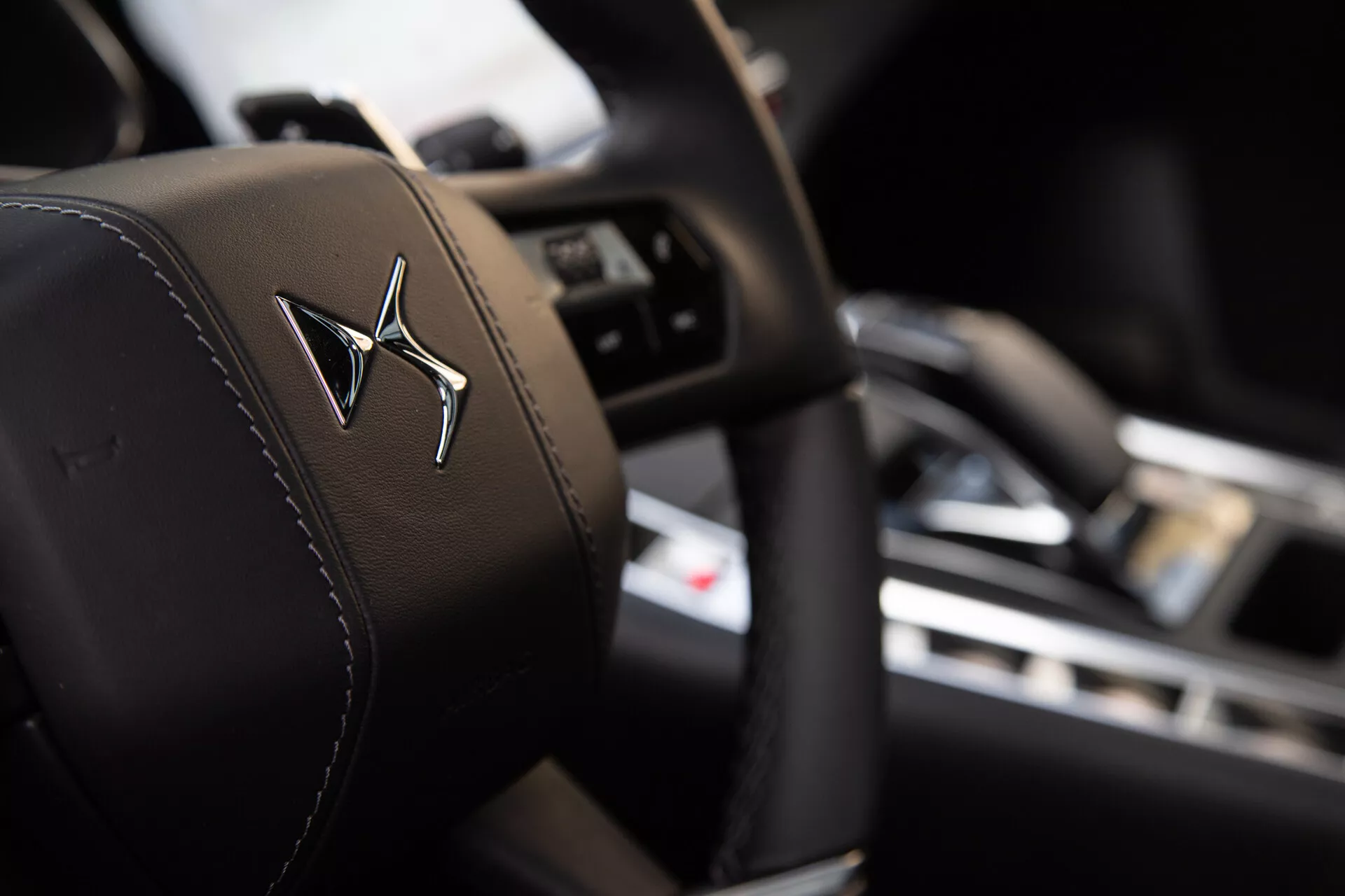 Vista detallada del reposacabezas del asiento del conductor con un logo grabado, con poca profundidad de campo que resalta el reposacabezas en un enfoque nítido contra un fondo interior borroso mostrando un volante con botones de control y un tablero con pantalla central.