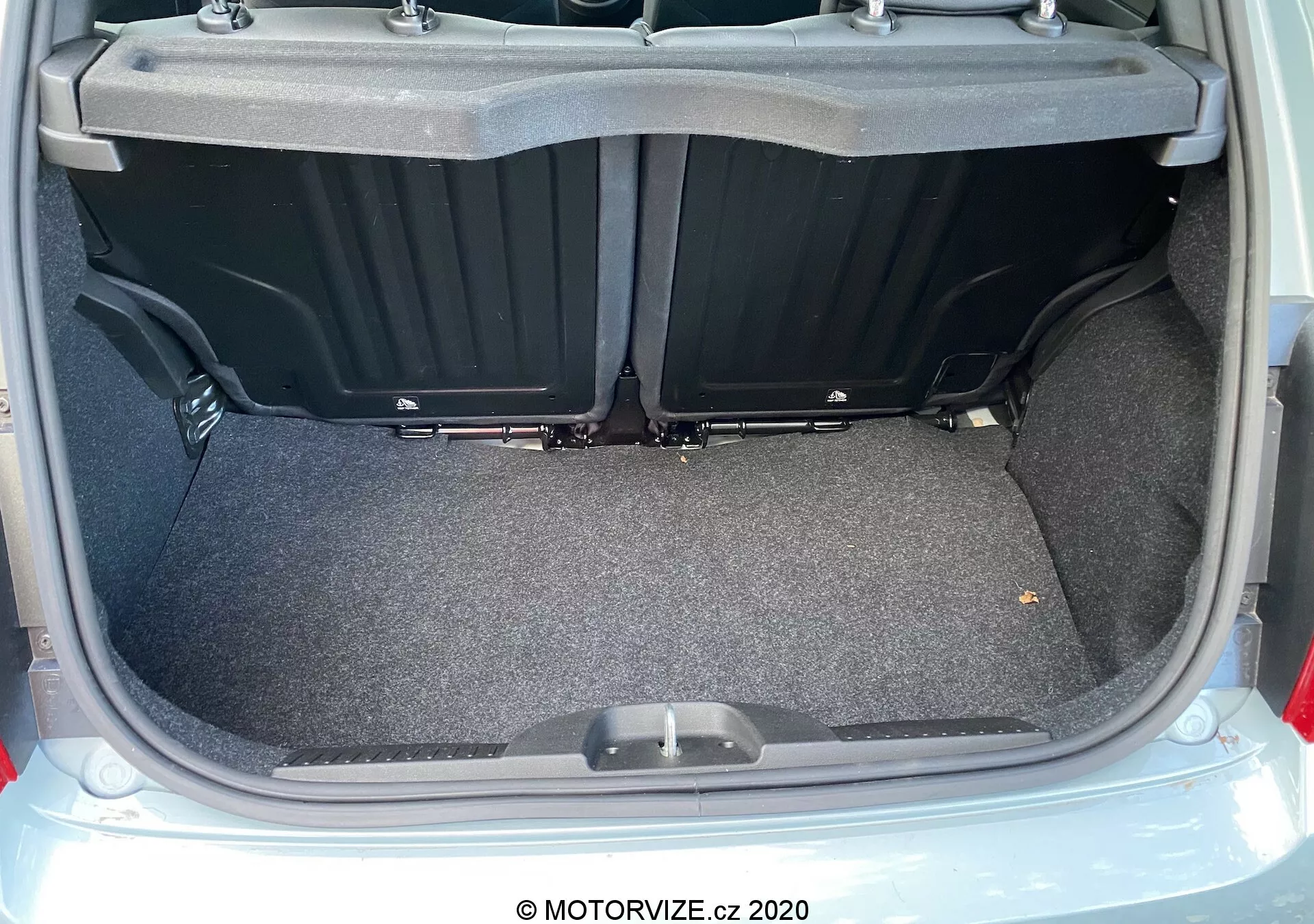 Vista de cerca del maletero del Fiat 500 de 2015 desde una perspectiva trasera con la tapa abierta, mostrando un área de carga alfombrada y plana con compartimentos laterales de plástico y un asa en el suelo del maletero. La imagen destaca la amplitud, usabilidad y el estado limpio y bien iluminado del maletero.