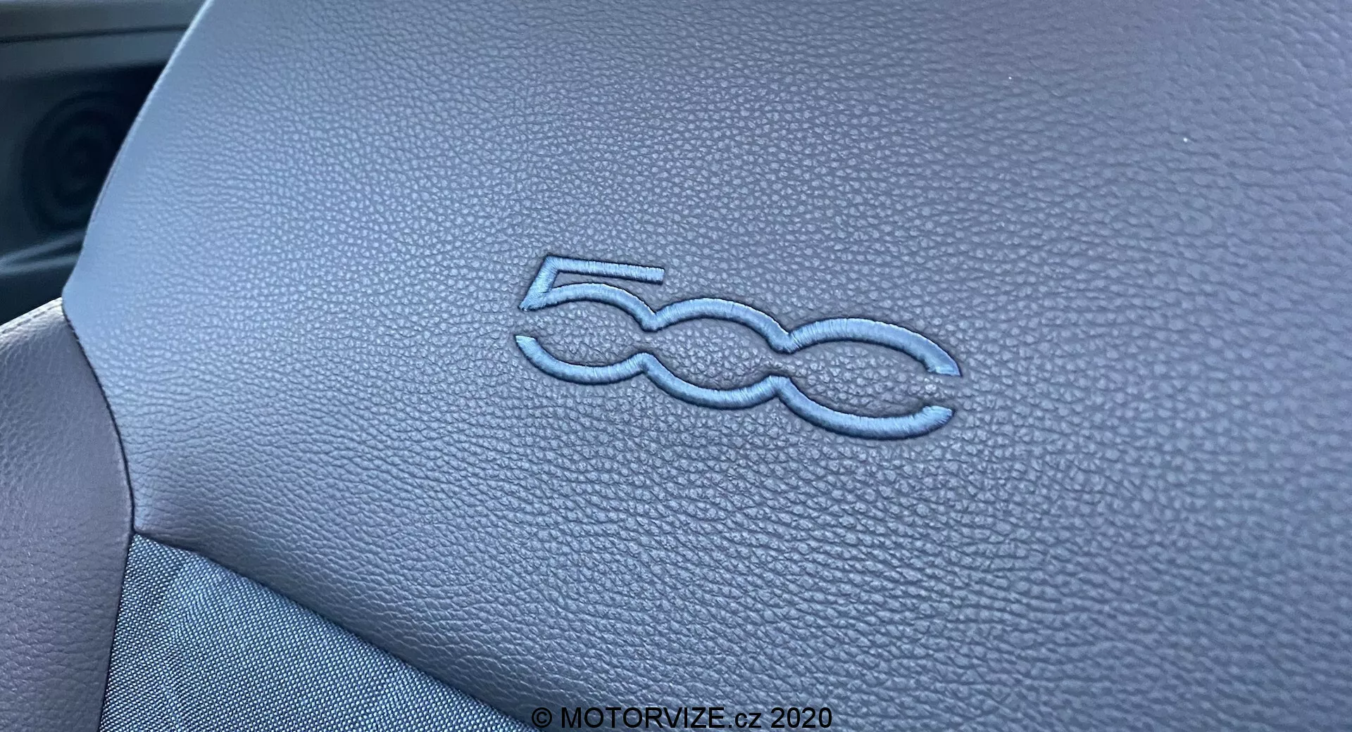 Imagen de primer plano que muestra el logo '500' elegantemente grabado en el tablero del interior del Fiat 500 2015. La textura similar al cuero y la costura precisa del panel del tablero se destacan gracias a la iluminación y la profundidad de campo estrecha, resaltando la alta calidad de la artesanía del diseño interior del vehículo.
