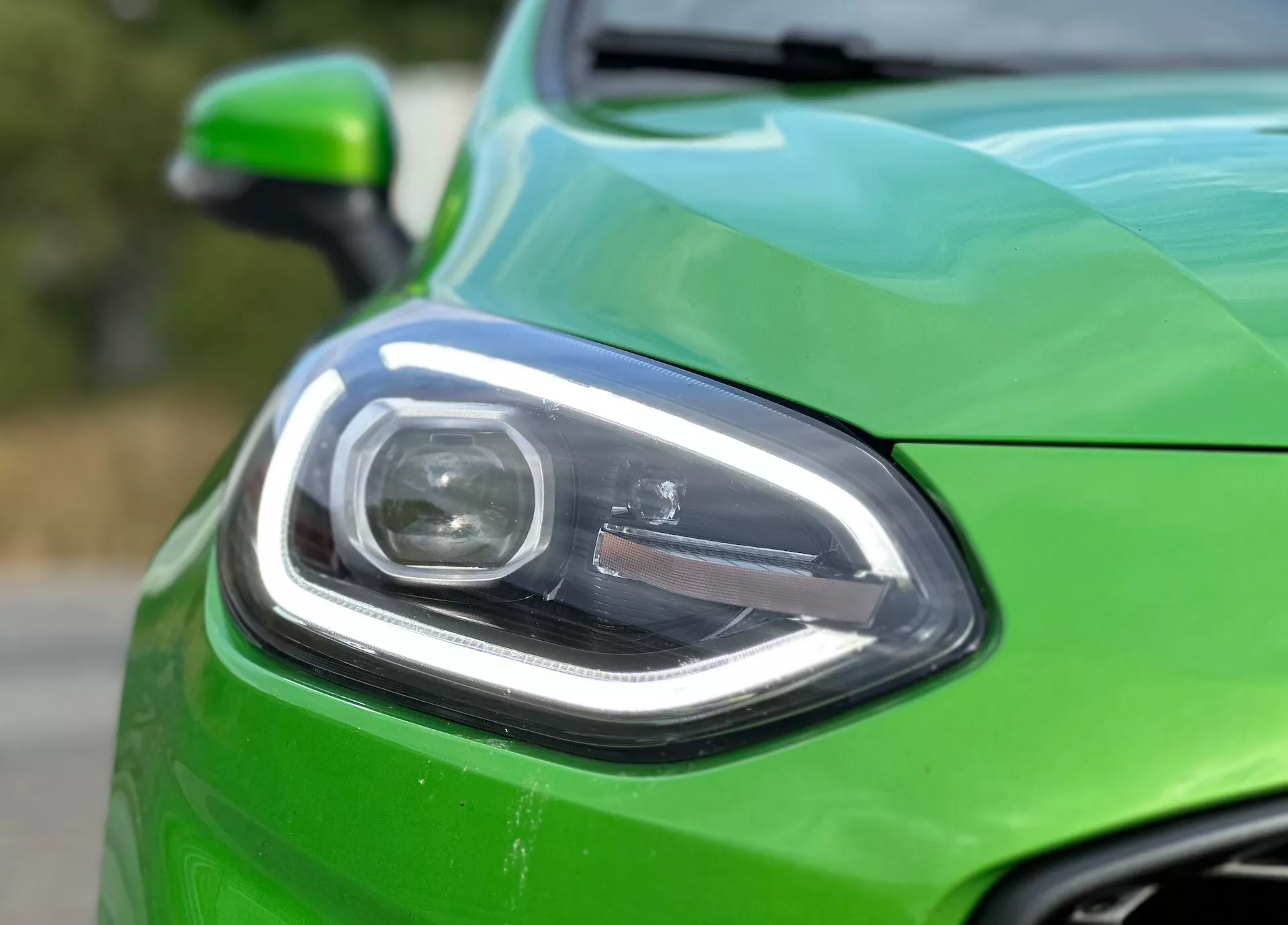 Vista detallada del frente izquierdo de un Ford Fiesta 2022 en verde vibrante, mostrando el diseño moderno del faro, parte de la parrilla y acabado brillante con fondo desenfocado que enfatiza los detalles del diseño del vehículo y la tecnología de iluminación avanzada.