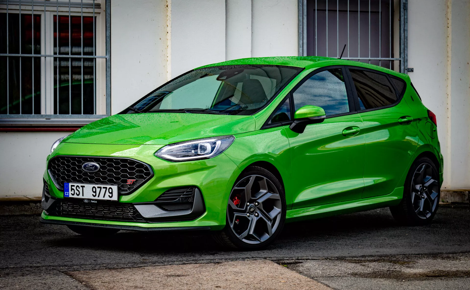 Ford Fiesta verde brillante modelo hatchback moderno 2022 enfatizando estatura deportiva con parrilla frontal prominente y faros delanteros elegantes LED, aparcado en diagonal frente a un edificio