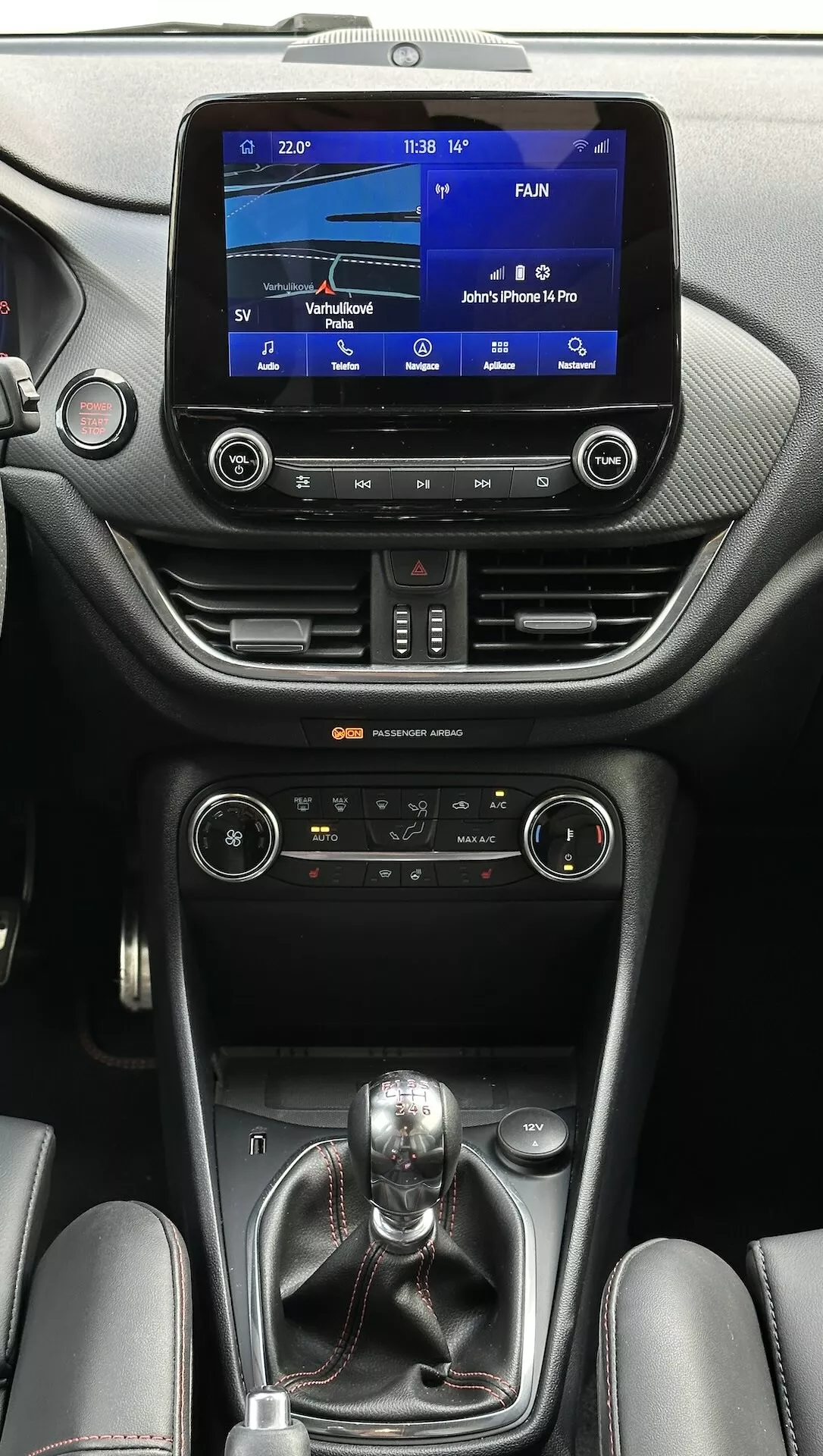 Interior del Ford Fiesta 2022 que muestra el sistema de infoentretenimiento táctil, controles climáticos duales, transmisión manual y acentos de lujo en cuero vistos desde el lado del pasajero