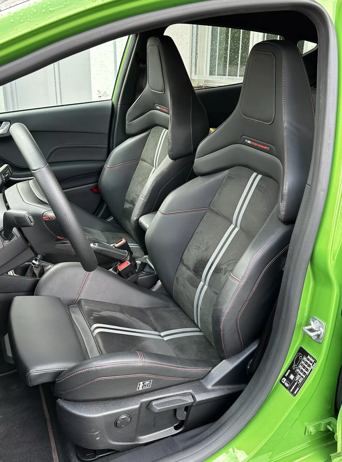 Vista detallada del asiento del conductor deportivo con tapicería de cuero y ribete rojo, cinturón de seguridad de tres puntos y controles eléctricos del asiento, acentuado con un acabado interior verde en el Ford Fiesta 2022.