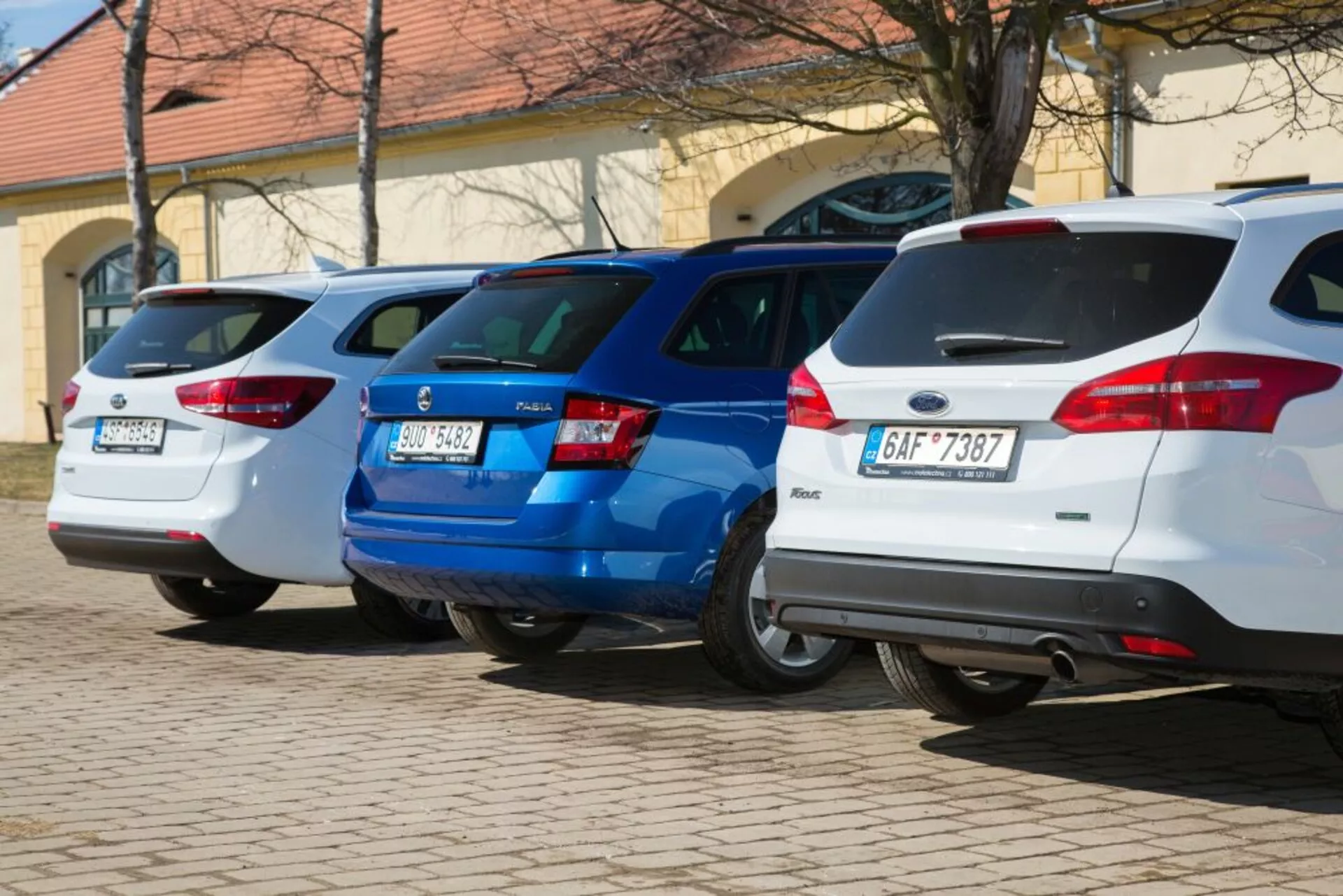 Una alineación de tres hatchbacks, incluido un Ford Focus blanco del año 2011, aparcados perpendicularmente con las partes traseras enfrentadas a la cámara, mostrando las luces traseras y las características de diseño trasero en un área de estacionamiento bien iluminada.