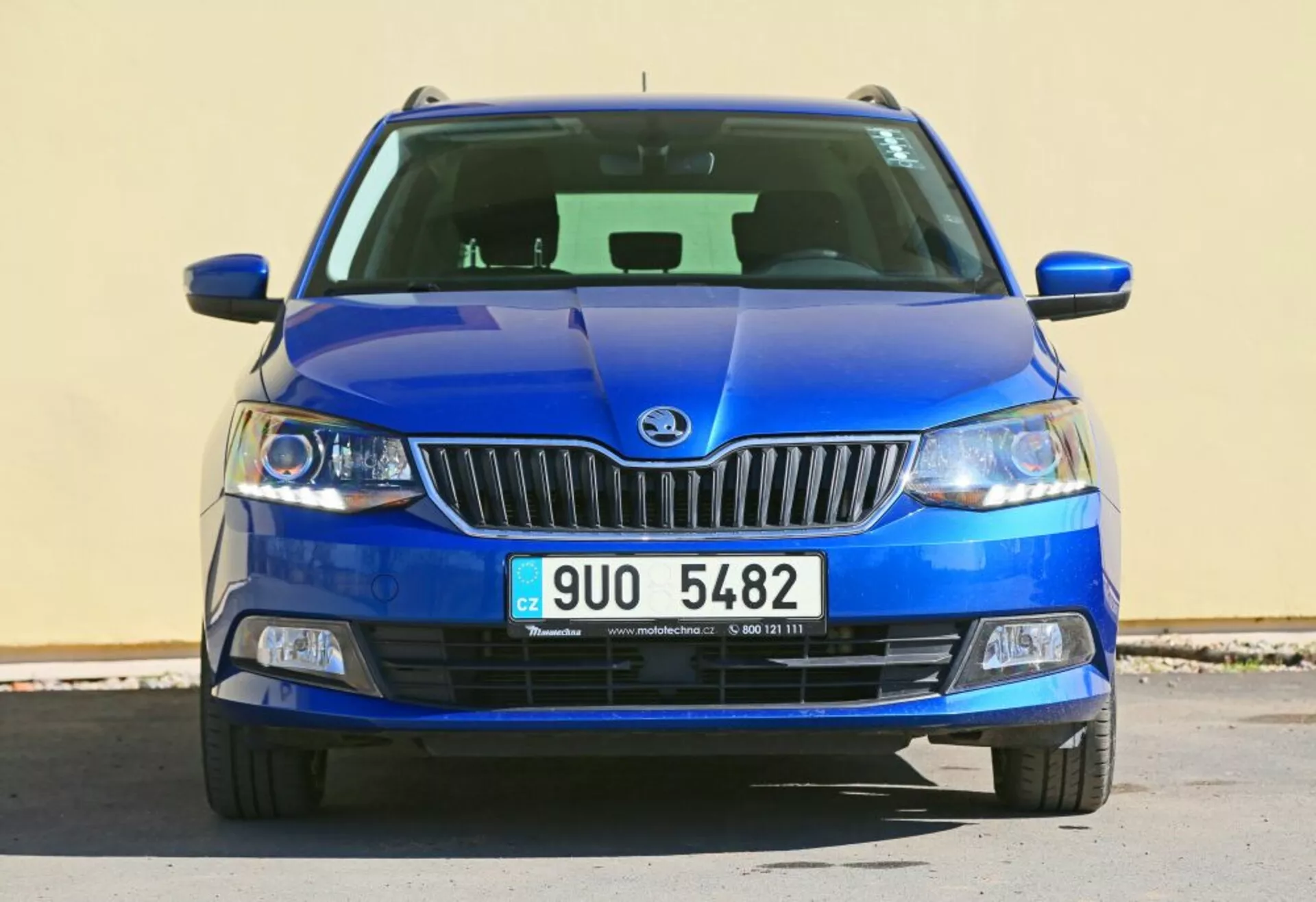 Vista frontal de un vehículo azul Škoda con el emblema de la marca en la parrilla cromada, faros con lentes transparentes y luces antiniebla en carcasa negra, con una rejilla inferior detallada y un diseño de capó esculpido.