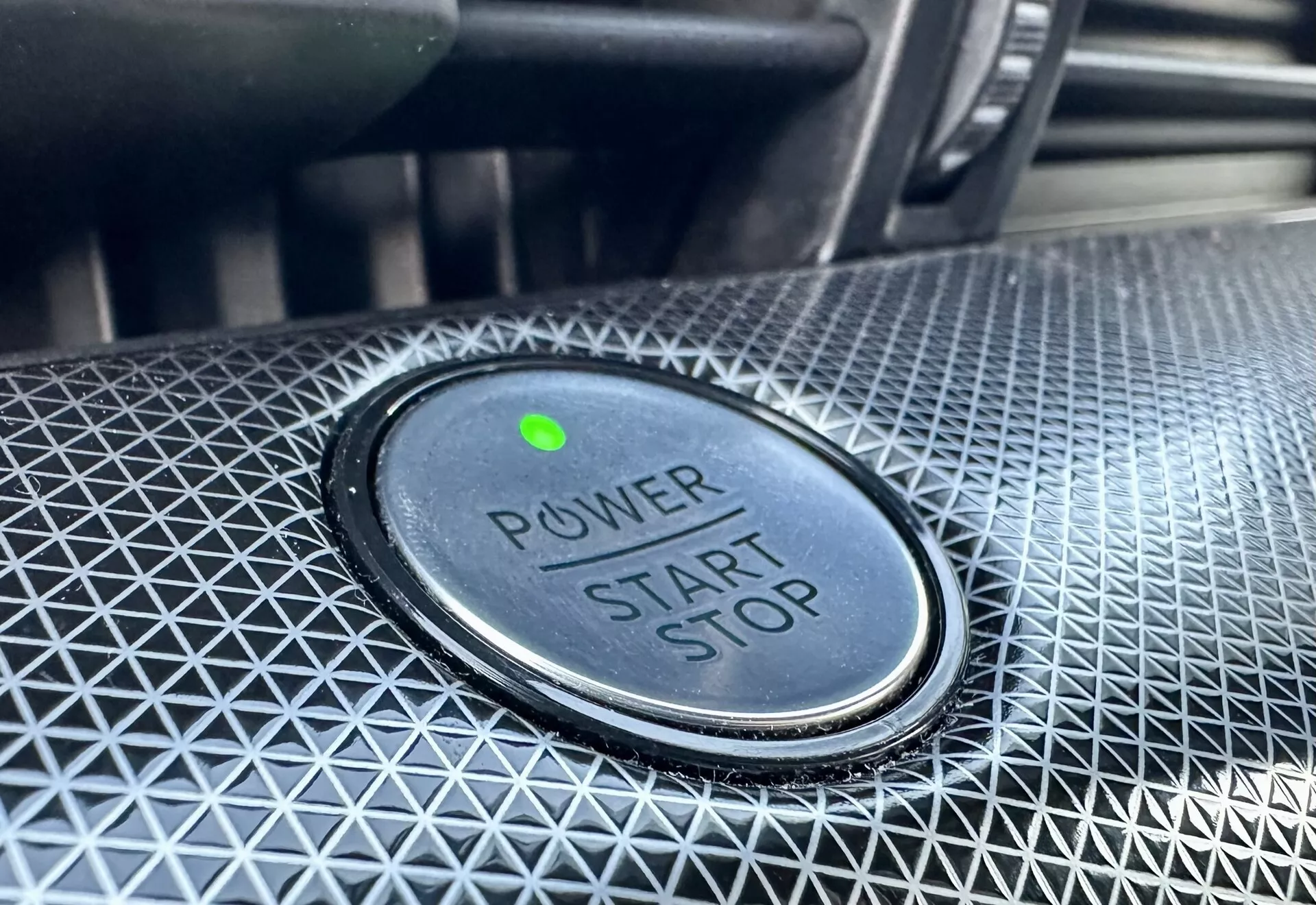 Vista en primer plano del botón de encendido/apagado en un Ford Mustang-Mach-E 2020, con el texto 'POWER START STOP', luz indicadora verde y diseño texturizado alrededor