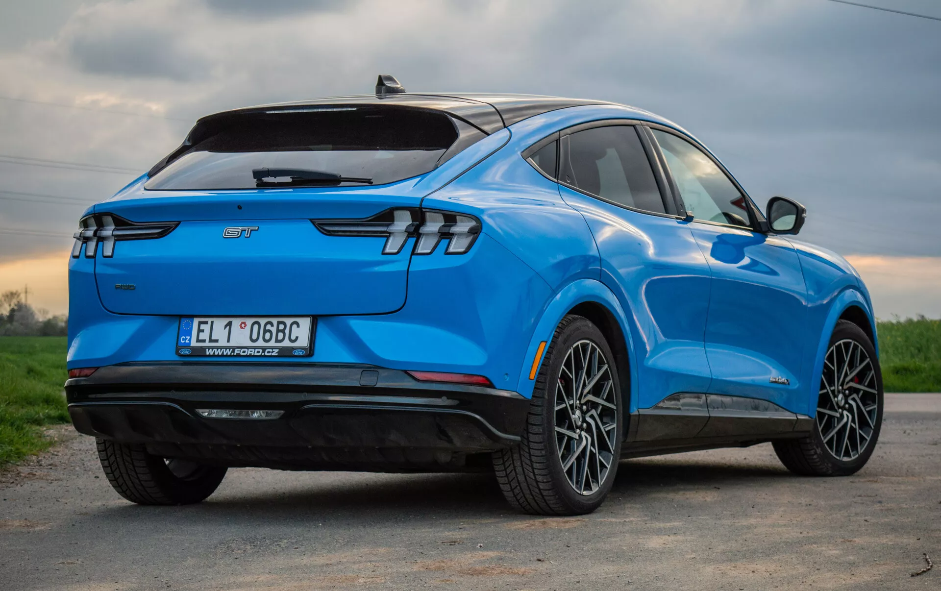 SUV eléctrico azul Ford Mustang Mach-E 2020 mostrado desde una perspectiva trasera de tres cuartos, resaltando su diseño aerodinámico elegante, luces traseras LED modernas, ruedas de aleación de múltiples radios, distintivo de vehículo eléctrico y características tecnológicas