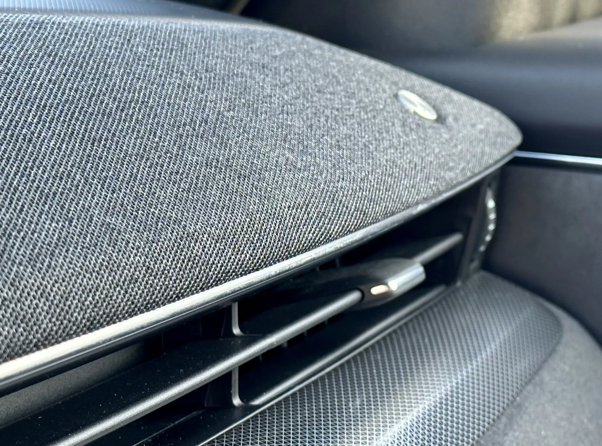 Vista detallada del interior del Ford Mustang Mach-E 2020 mostrando una parte del tablero o panel de la puerta con una rejilla de altavoz de tela de alta calidad integrada, un emblema que sugiere una asociación con un fabricante de equipos de audio de alta gama, junto a una rejilla de ventilación negra brillante