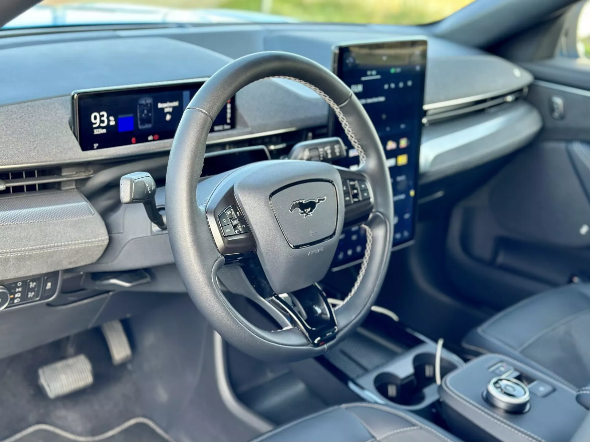 Vista interior de un Ford Mustang Mach-E 2020 enfocada en el cockpit del conductor desde la perspectiva del pasajero delantero, con un volante con emblema de Mustang, tablero digital en modo Park mostrando un rango de 93 millas, y una pantalla táctil central orientada verticalmente integrada con capacidades de infoentretenimiento avanzadas.