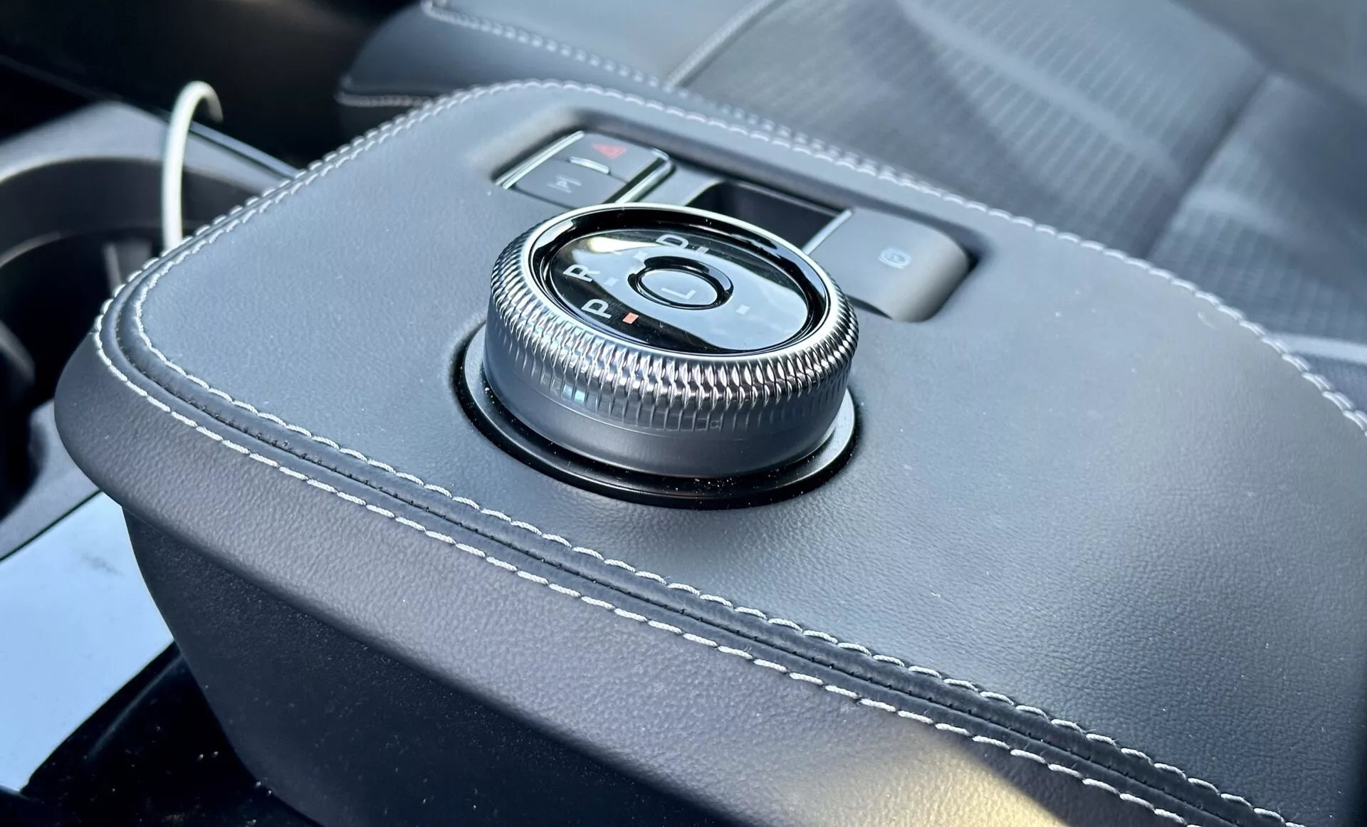 Vista en detalle del interior del Ford Mustang Mach-E 2020 con control giratorio en la consola central sobre una superficie revestida en cuero con costuras blancas, proporcionando una interfaz ergonómica para el sistema de infoentretenimiento