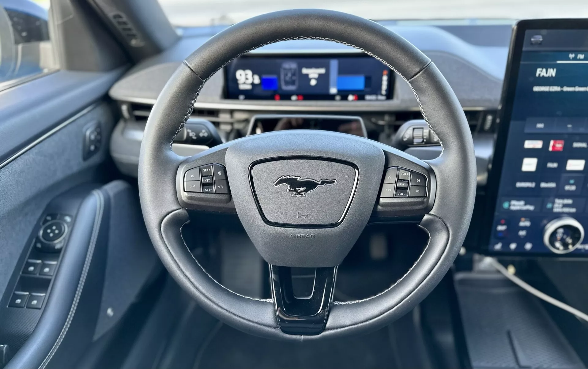 Vista interior de un Ford Mustang-Mach-E 2020 desde la perspectiva del conductor, mostrando un volante de tres radios con controles, un cuadro de instrumentos digital y una pantalla táctil de infoentretenimiento grande