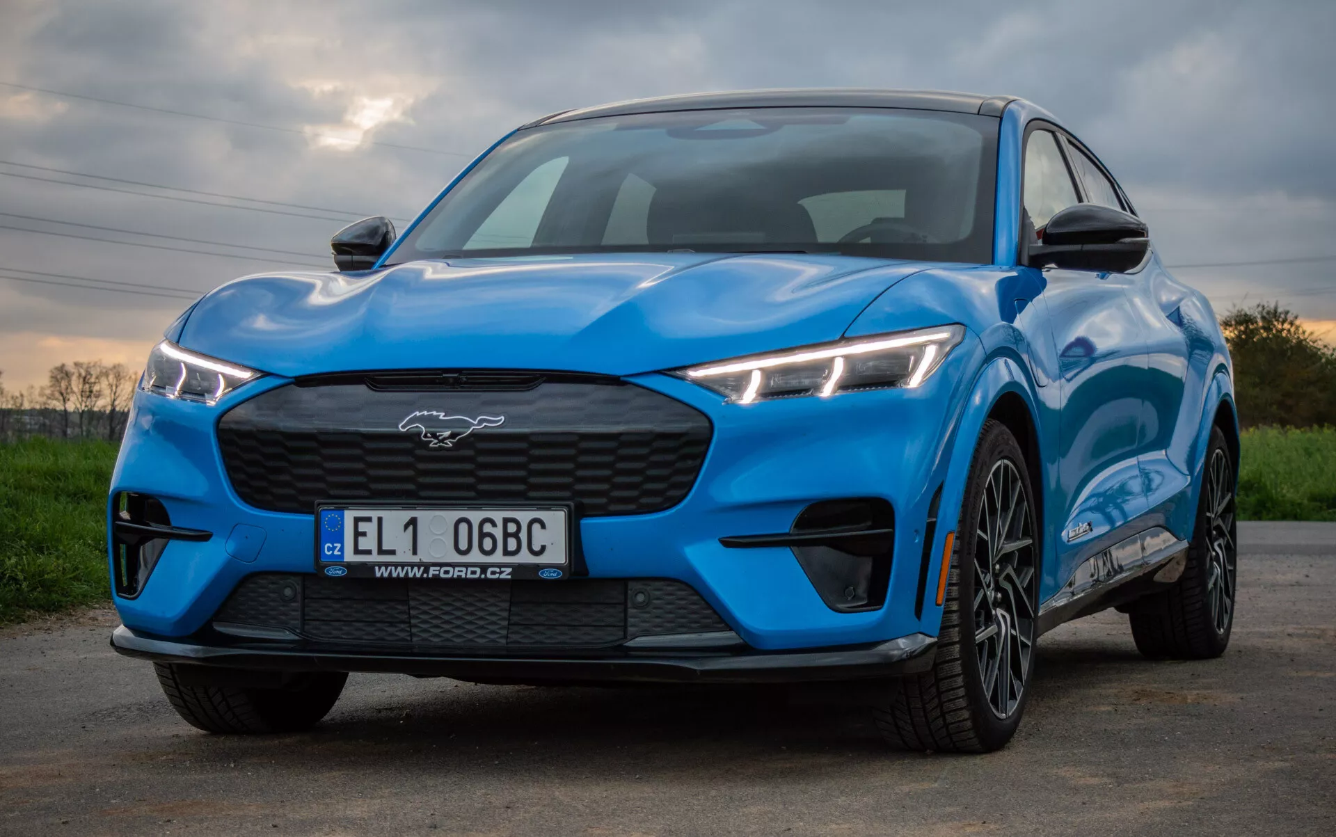 Ford Mustang Mach-E 2020 en azul brillante exhibiendo un diseño deportivo y aerodinámico desde una perspectiva delantera y lateral baja, destacando faros LED angulares, parrilla cerrada, capó contorneado y ruedas de aleación de múltiples radios contra un fondo natural.