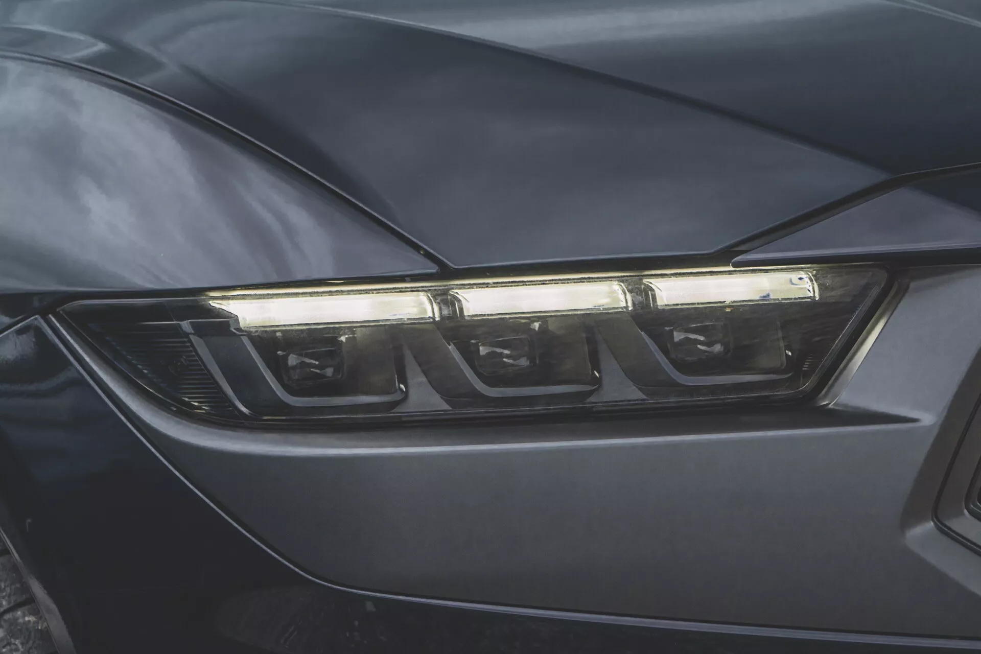 Primer plano del faro del lado del conductor del Ford Mustang 2024, ilustrando la tecnología moderna LED o HID y un diseño aerodinámico en un acabado de color oscuro.