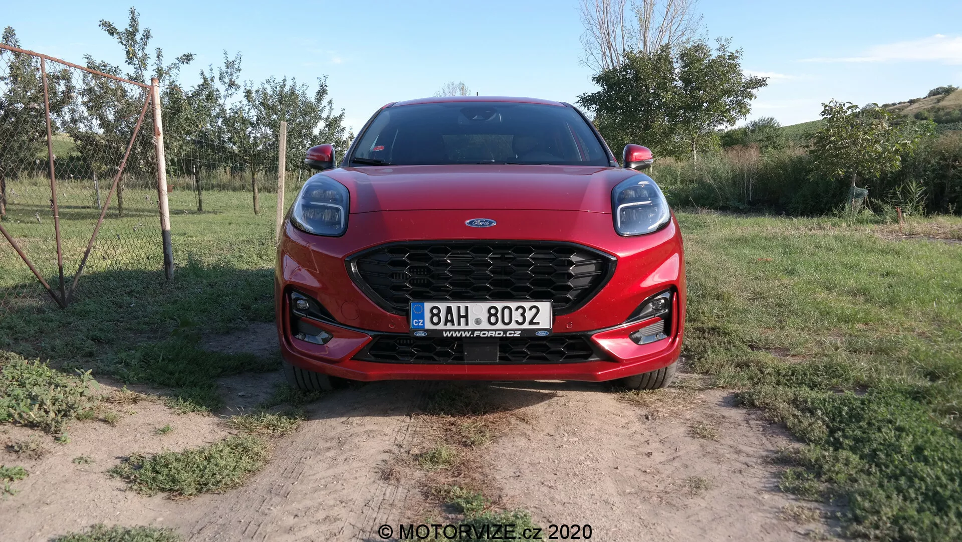 Vista frontal de un Ford Puma 2020 que muestra su parrilla de malla prominente, faros LED elegantes y contornos aerodinámicos del capó. El coche está situado sobre tierra seca con parches de hierba, sugiriendo un entorno rural.