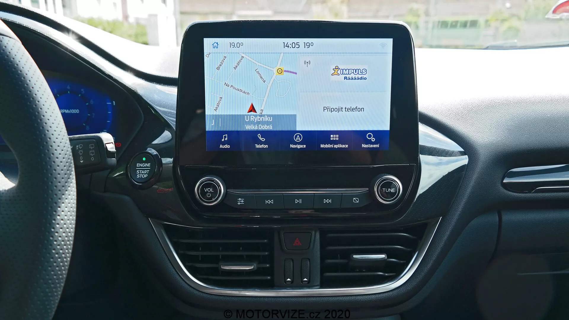 Consola central del interior del Ford Puma 2020 desde la perspectiva del conductor o pasajero delantero, mostrando el sistema de infoentretenimiento con pantalla táctil que muestra el mapa de navegación, botones físicos para luces de emergencia, ajustes de control de clima, ranura para CD, puerto USB y toma de corriente de 12V. La consola también cuenta con termómetro digital que indica 17°C y reloj que muestra 14:05, todo rodeado de elementos de diseño interior moderno con líneas curvas y ventilaciones de aire acondicionado.