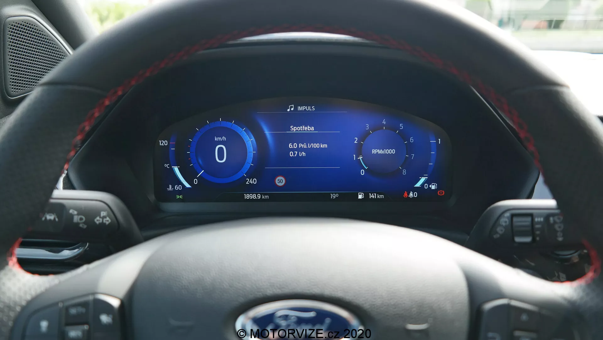 Vista interior del Ford Puma 2020 desde el asiento del conductor, con un volante de cuero con botones multifunción y un panel de instrumentos digital de alta resolución. La pantalla muestra velocidad, navegación, métricas del vehículo, indicador de nivel de batería sugiriendo capacidades híbridas/eléctricas y controles para medios y control de crucero.