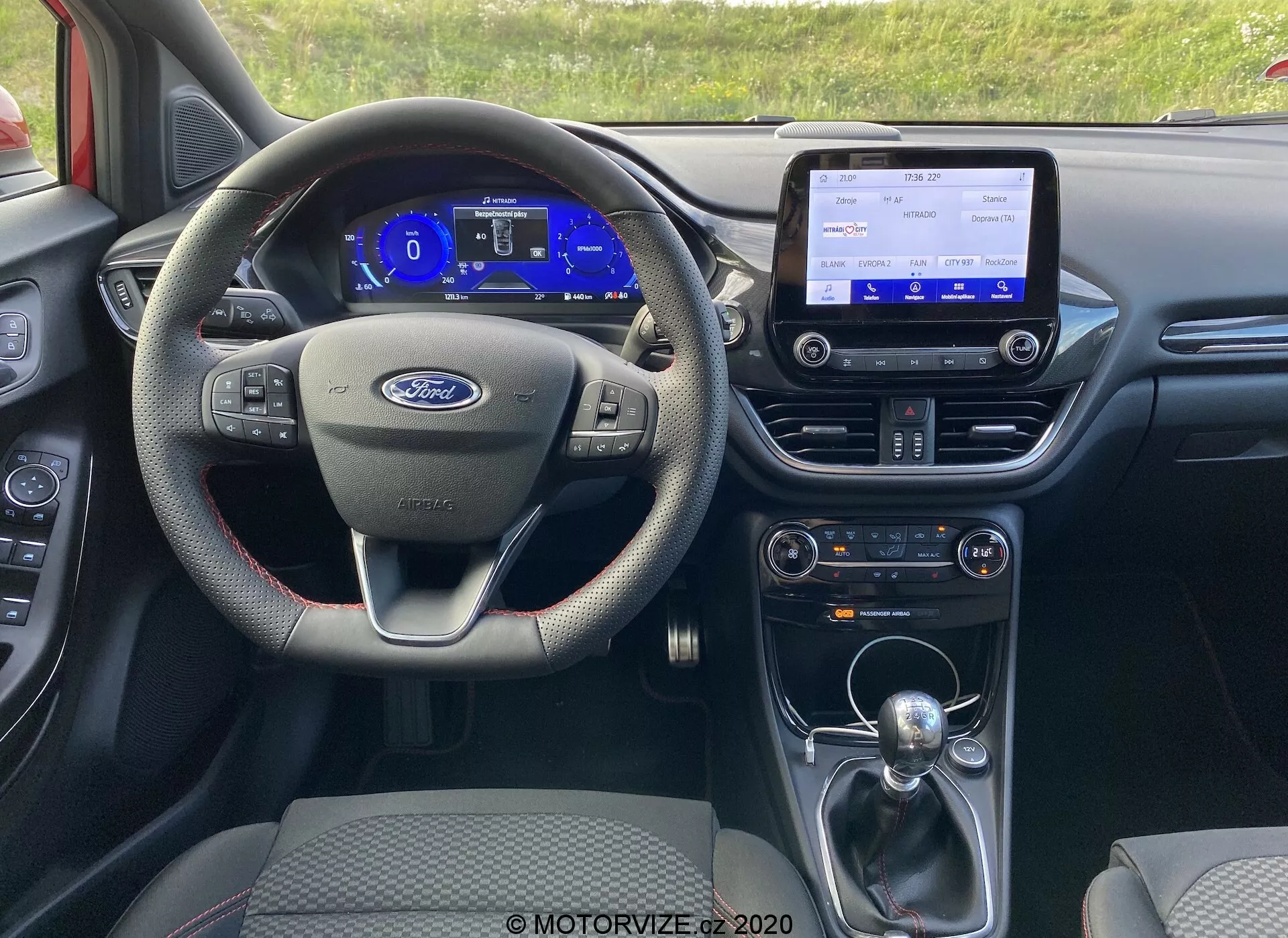 Toma interior del Ford Puma 2020 desde la perspectiva del conductor, mostrando el volante multifuncional de tres radios, el cuadro de instrumentos digital, la consola central de información y entretenimiento con funciones de conectividad, la palanca de cambio de transmisión automática y varios sistemas de control