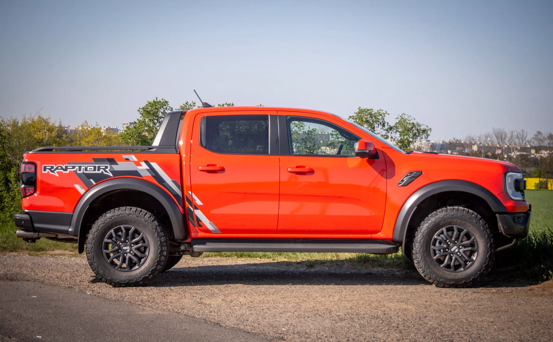 Ford Ranger Raptor 2022 en naranja brillante, mostrando un estilo agresivo, capacidades todoterreno con grandes llantas negras y neumáticos de banda profunda, aparcado en una superficie pavimentada junto a césped durante el día