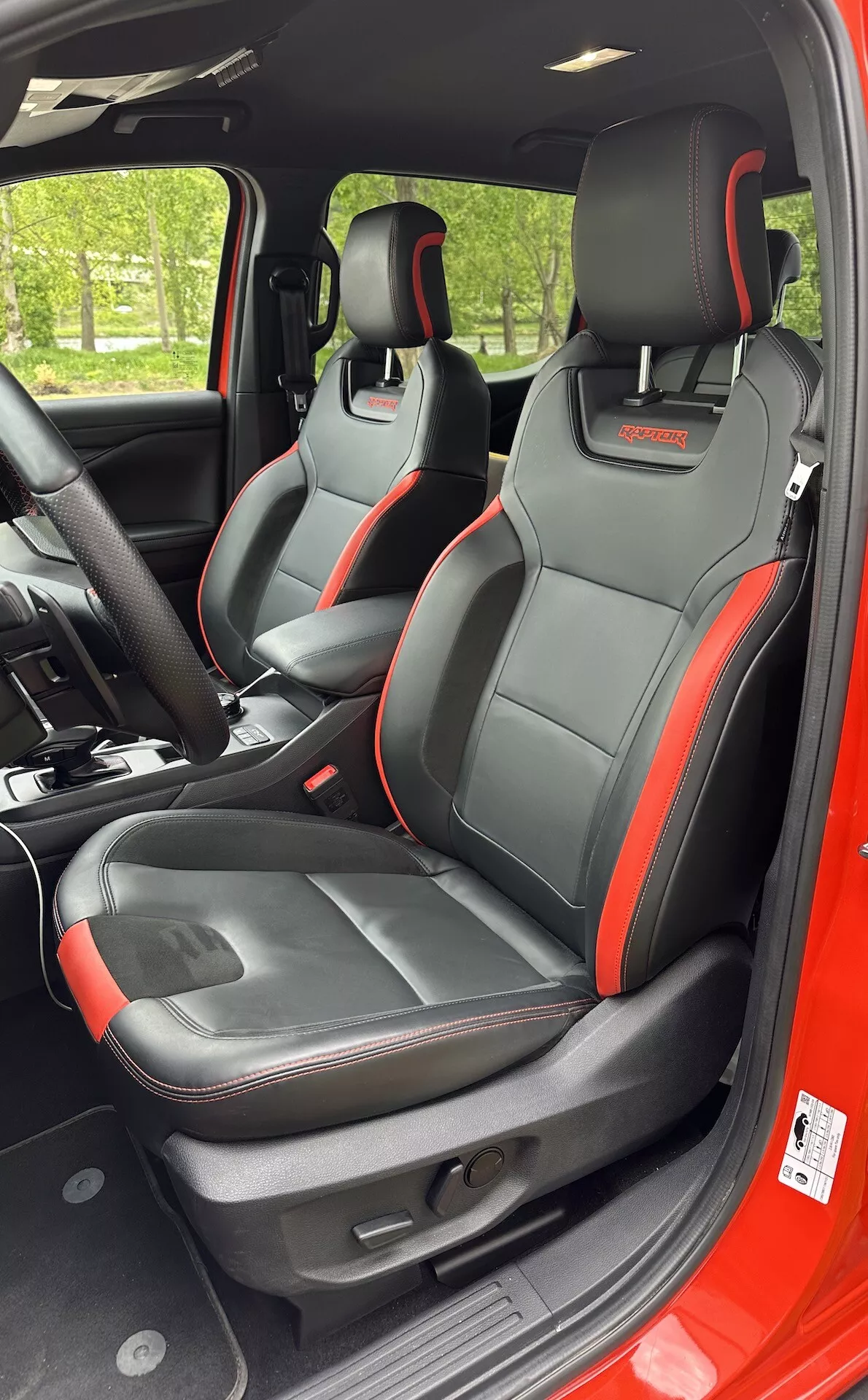 Vista interior del Ford Ranger 2022 enfocándose en asientos delanteros deportivos con ribete acentuado en negro y rojo, características integradas en los reposacabezas y ajustes eléctricos de asientos desde una perspectiva lateral derecha