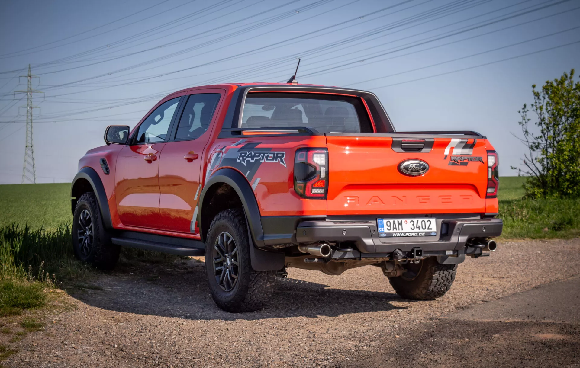 Camioneta Ford Ranger Raptor 2022 exhibida en un camino de grava, mostrando su robusto ángulo trasero de tres cuartos con enfoque en capacidades todoterreno y acabado de pintura naranja vibrante.