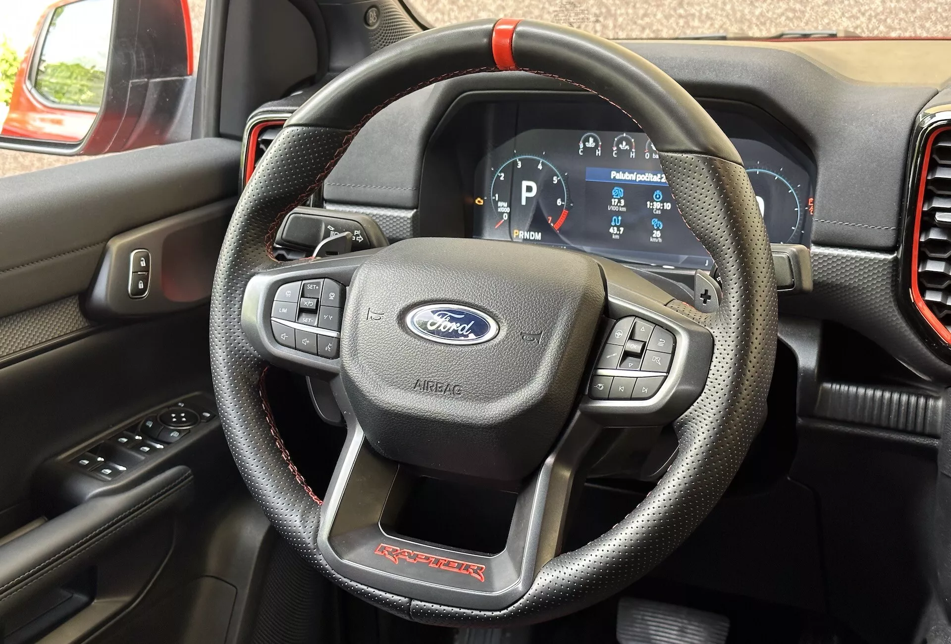 Vista detallada del interior de un Ford Ranger Raptor 2022 centrado en el volante similar al cuero con costuras rojas y controles multifunción, y el cuadro de instrumentos digital mostrando el vehículo en modo Park.