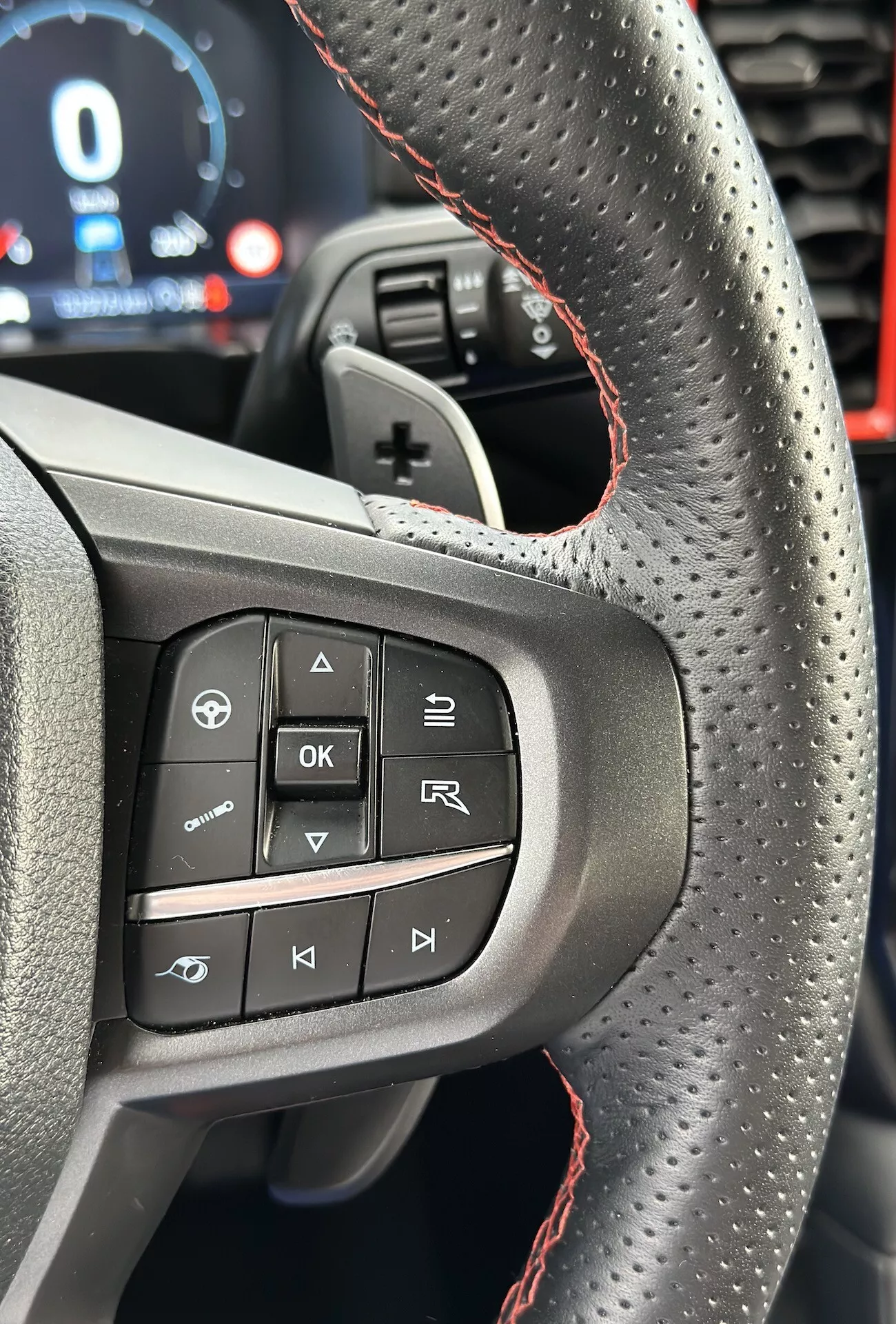 Primer plano del volante del Ford Ranger 2022 destacando los botones y características del lado izquierdo, incluyendo cuero perforado con costuras rojas, desde la perspectiva del conductor en orientación vertical