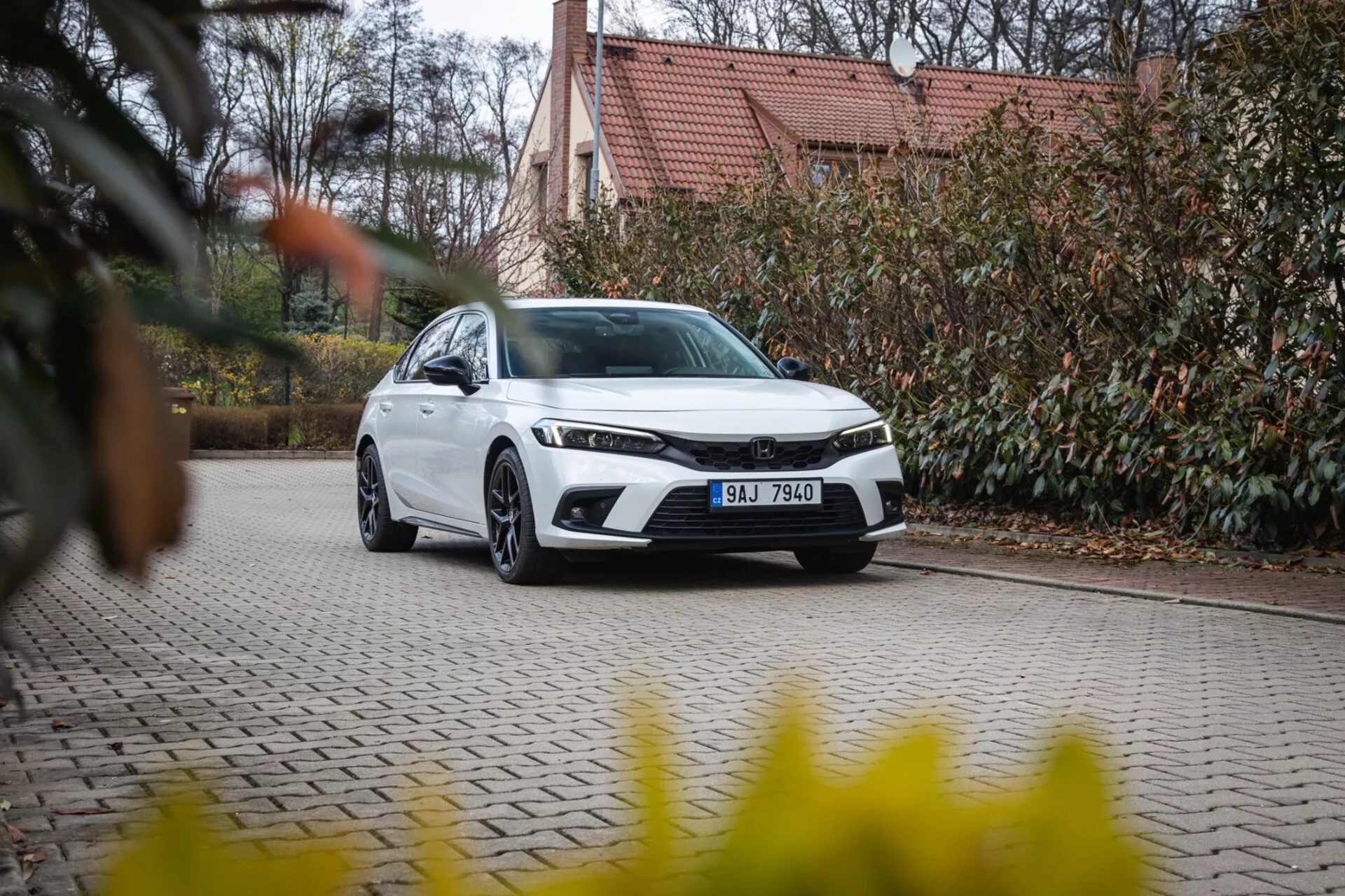Sedán moderno Honda Civic 2022 estacionado en un camino de adoquines con paisajismo y un edificio al fondo, mostrando la parrilla frontal, faros LED y diseño aerodinámico elegante