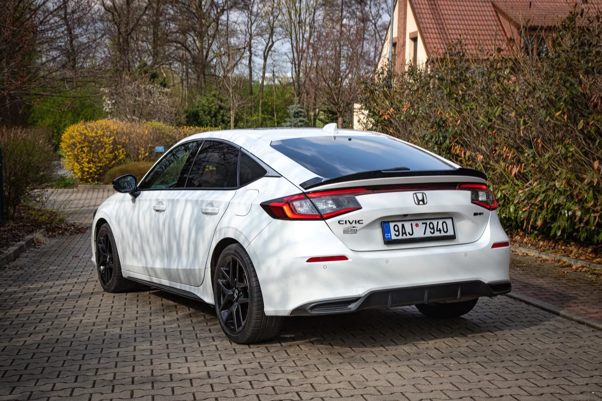 Honda Civic blanco 2022 mostrando perfil trasero y lateral parcial en un camino de ladrillos, con línea de techo inclinada, spoiler integrado, luz de freno LED, luces traseras distintivas y paragolpes deportivo con difusor