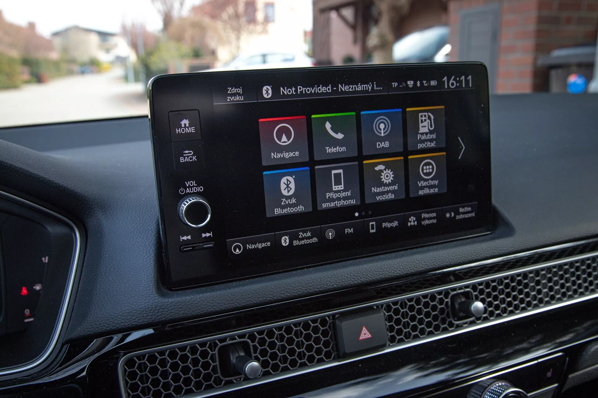 Interior del Honda Civic 2022 mostrando el moderno sistema de infoentretenimiento táctil con navegación, íconos de reproducción de audio y medios, conectividad telefónica, DAB, estado del vehículo, opciones de configuración de Bluetooth y del vehículo, contra un tablero texturizado con patrón de panal.