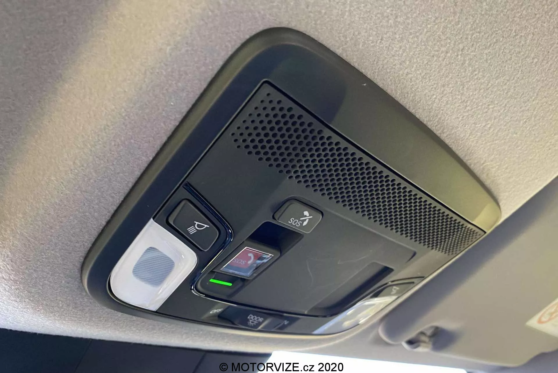 Vista de cerca de la consola superior del Honda Jazz 2020 (Jazz Crosstar). La imagen revela una serie de botones funcionales que incluyen controles de luz interior, un posible botón de desbloqueo de puerta, un área ventilada con un micrófono para llamadas manos libres, un home link con botones de apertura de garaje programables y un posible compartimento para gafas de sol o cierre de almacenamiento. La consola está capturada a la luz del día con enfoque claro en los botones texturizados, destacando la tecnología avanzada y el diseño interior del vehículo.