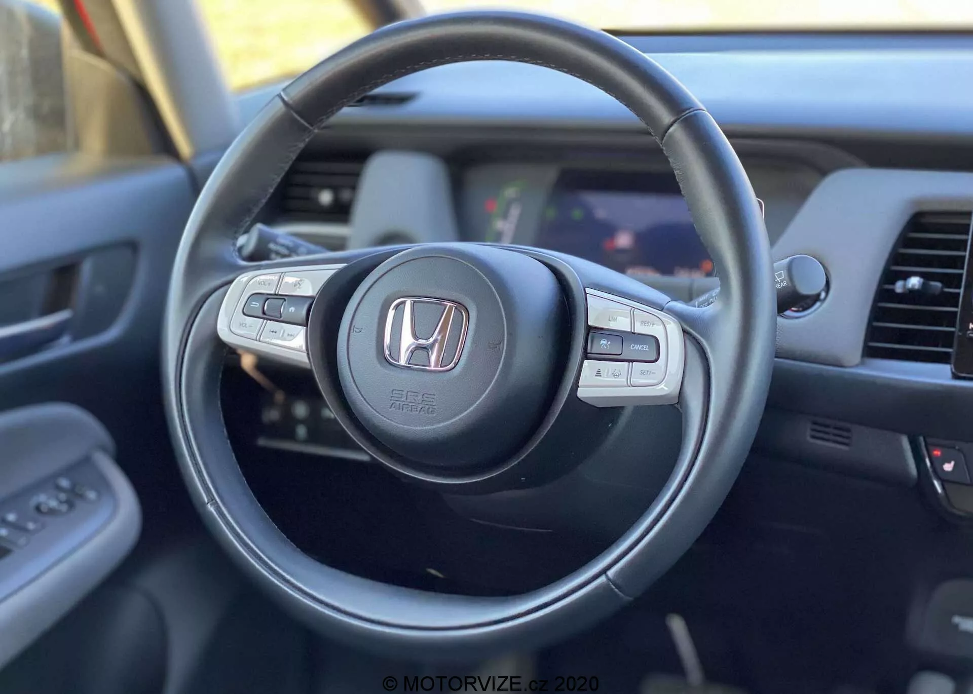 Vista interior del Honda Jazz Crosstar 2020 desde la perspectiva del conductor centrada en el volante moderno con logo Honda, con botones de control multifunción para audio, control de crucero y llamadas manos libres, y una vista parcial del salpicadero y el sistema de infoentretenimiento.