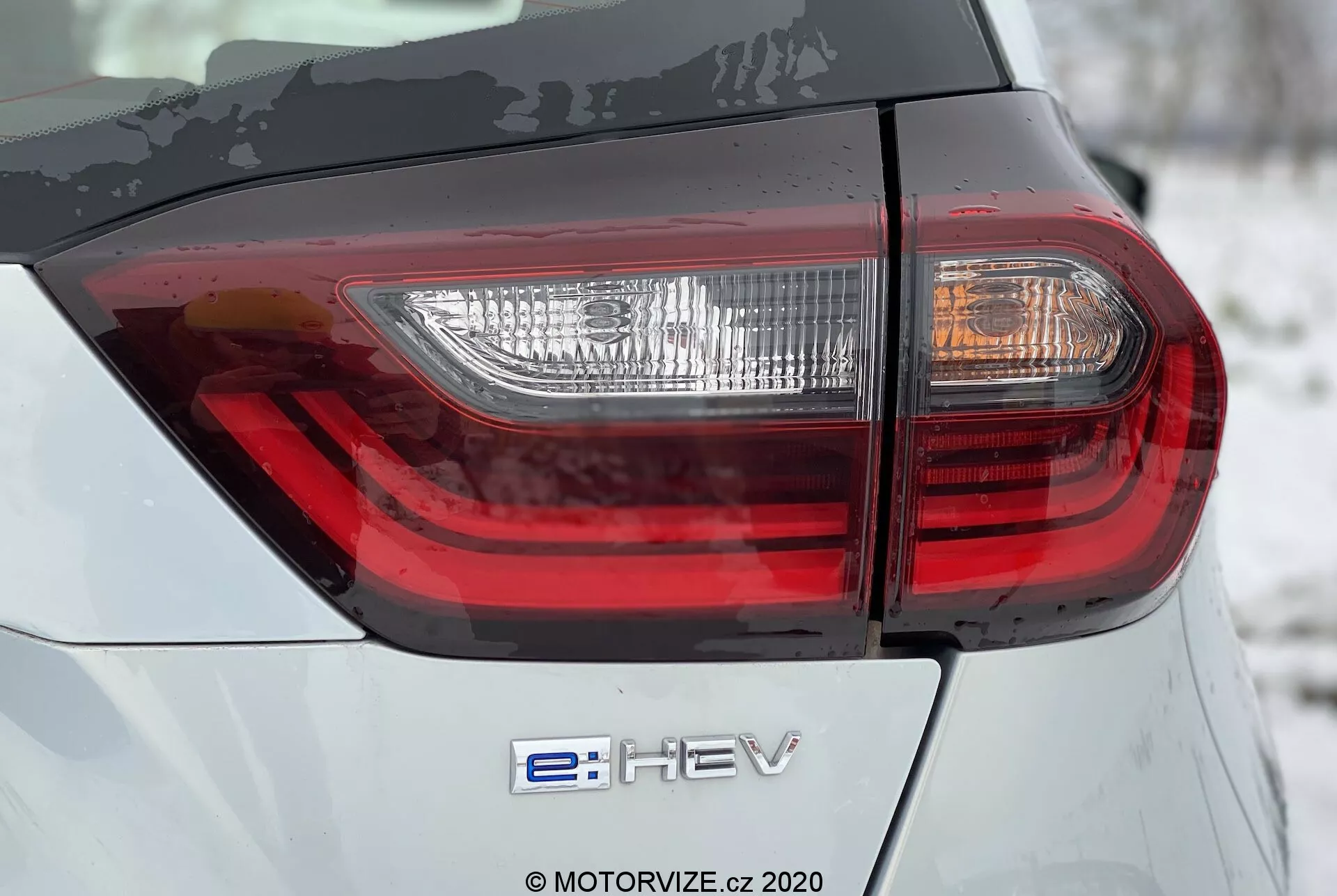 Honda Jazz 2020 Acercamiento Trasero: Con el Emblema Híbrido 'e:HEV' y Moderna Luz Trasera LED. La imagen resalta la carrocería plateada-gris con diseño de luz trasera intrincado desde un ángulo bajo de 45 grados.